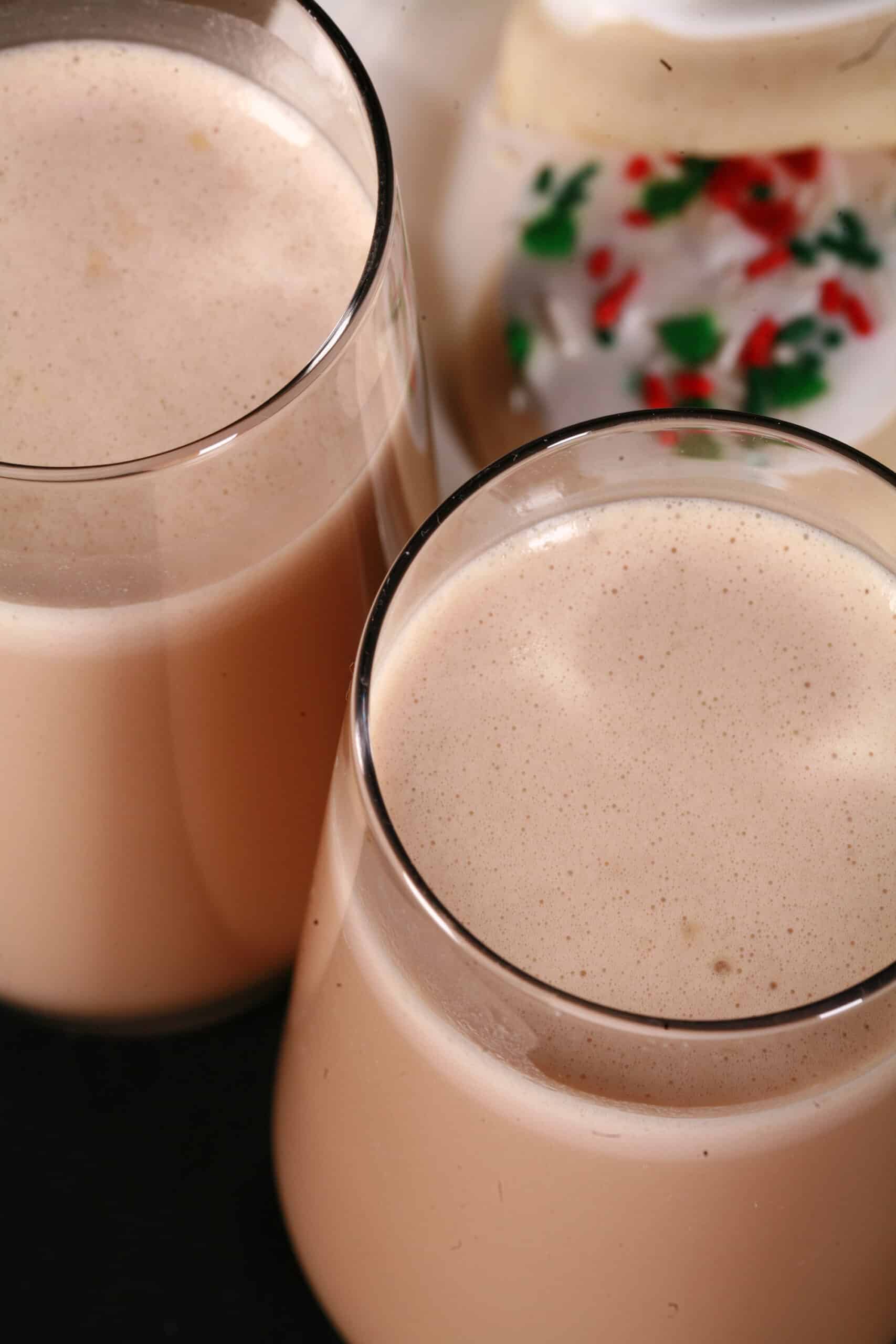 2 tall glasses of sugar cookie protein shakes, with frosted sugar cookies on a plate next to them.