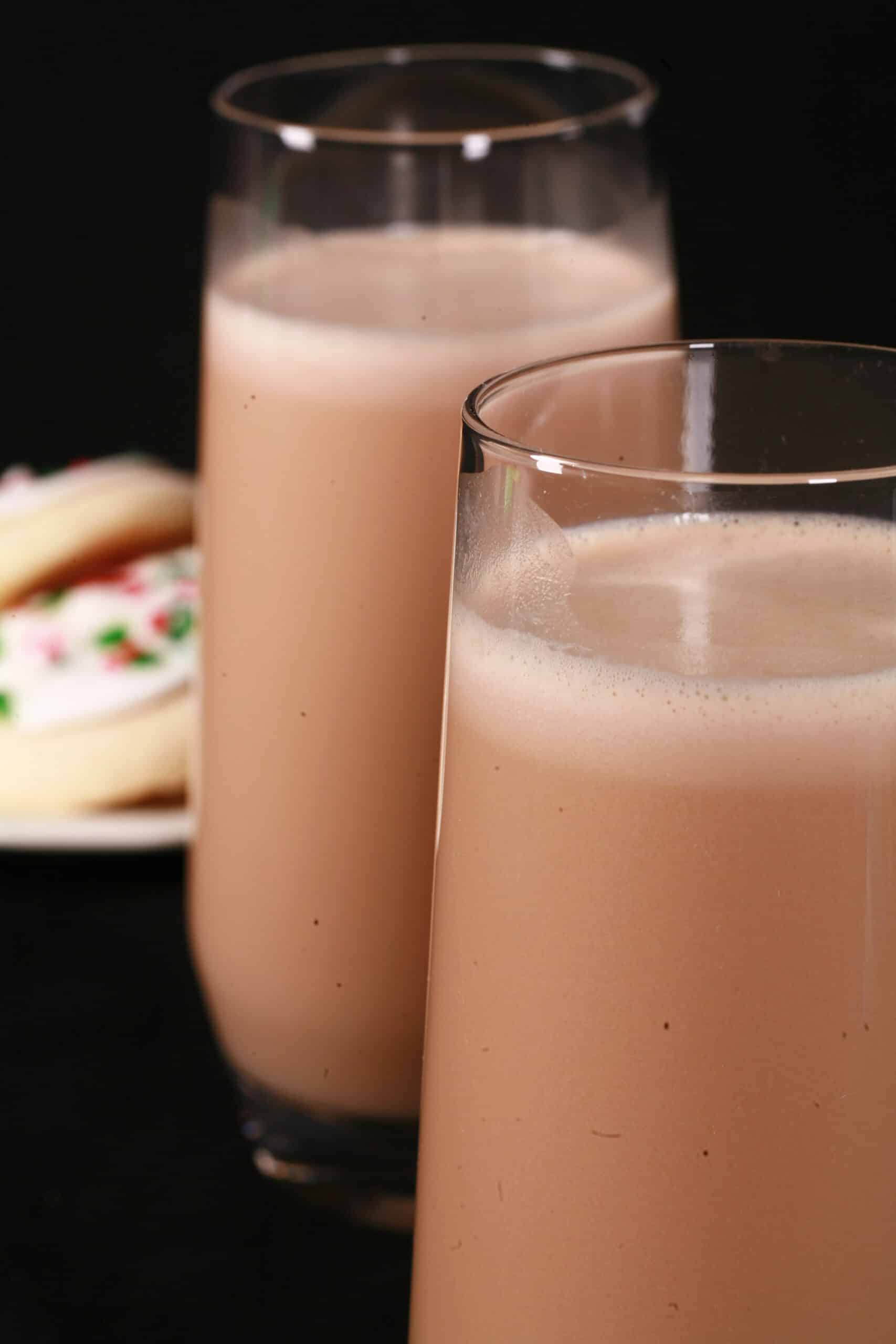 2 tall glasses of sugar cookie flavoured protein coffee shake, with frosted sugar cookies on a plate next to them.
