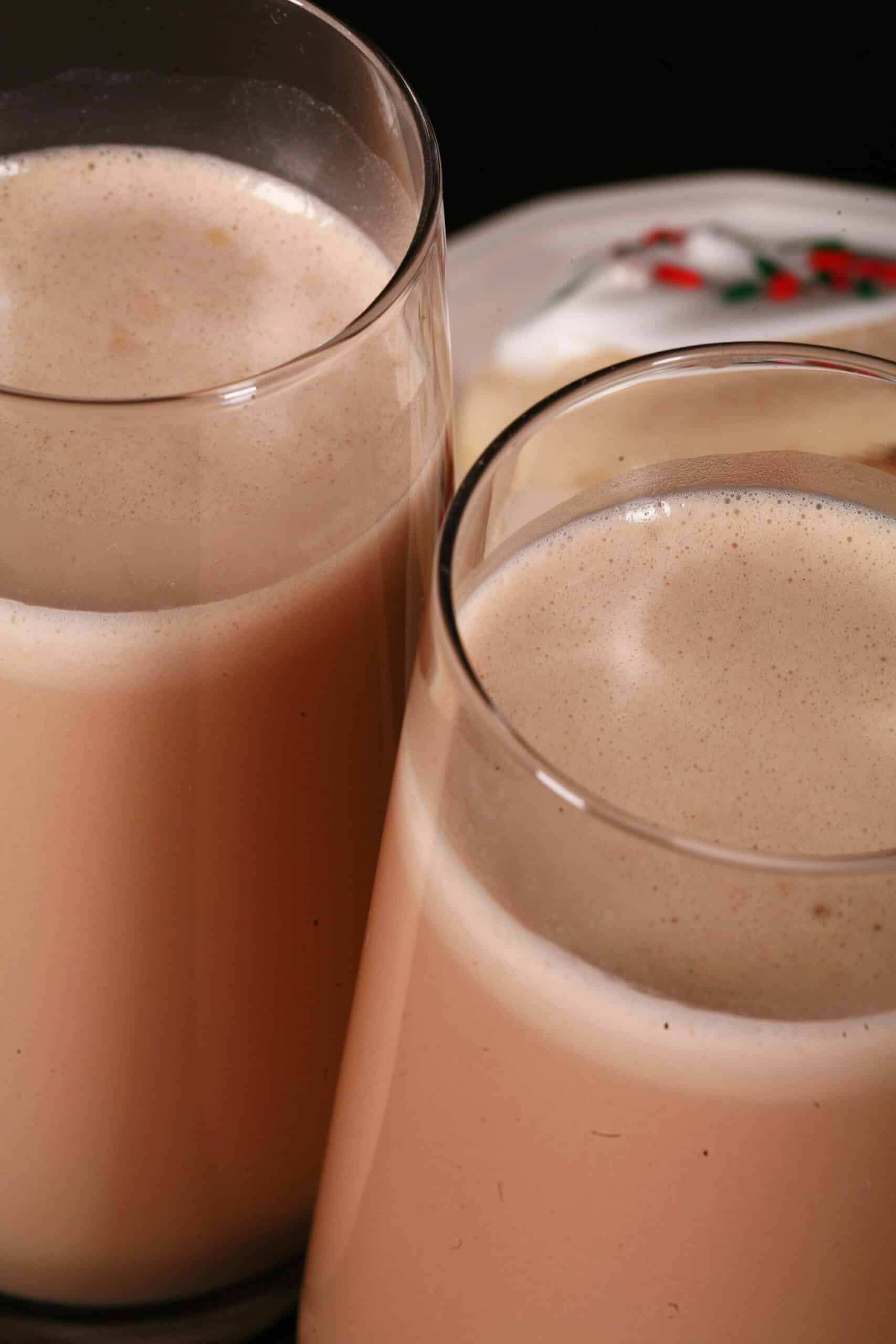 2 tall glasses of sugar cookie protein shakes, with frosted sugar cookies on a plate next to them.