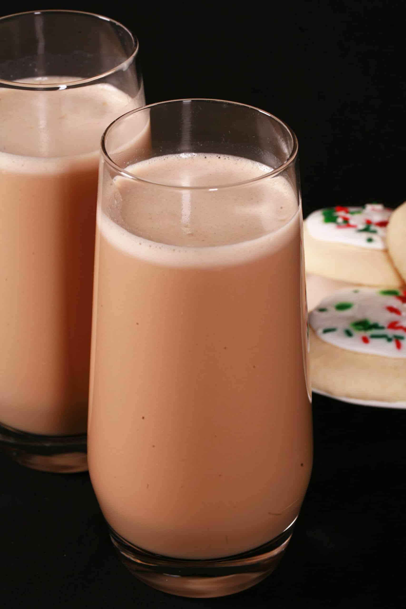 2 tall glasses of sugar cookie flavoured protein coffee shake, with frosted sugar cookies on a plate next to them.