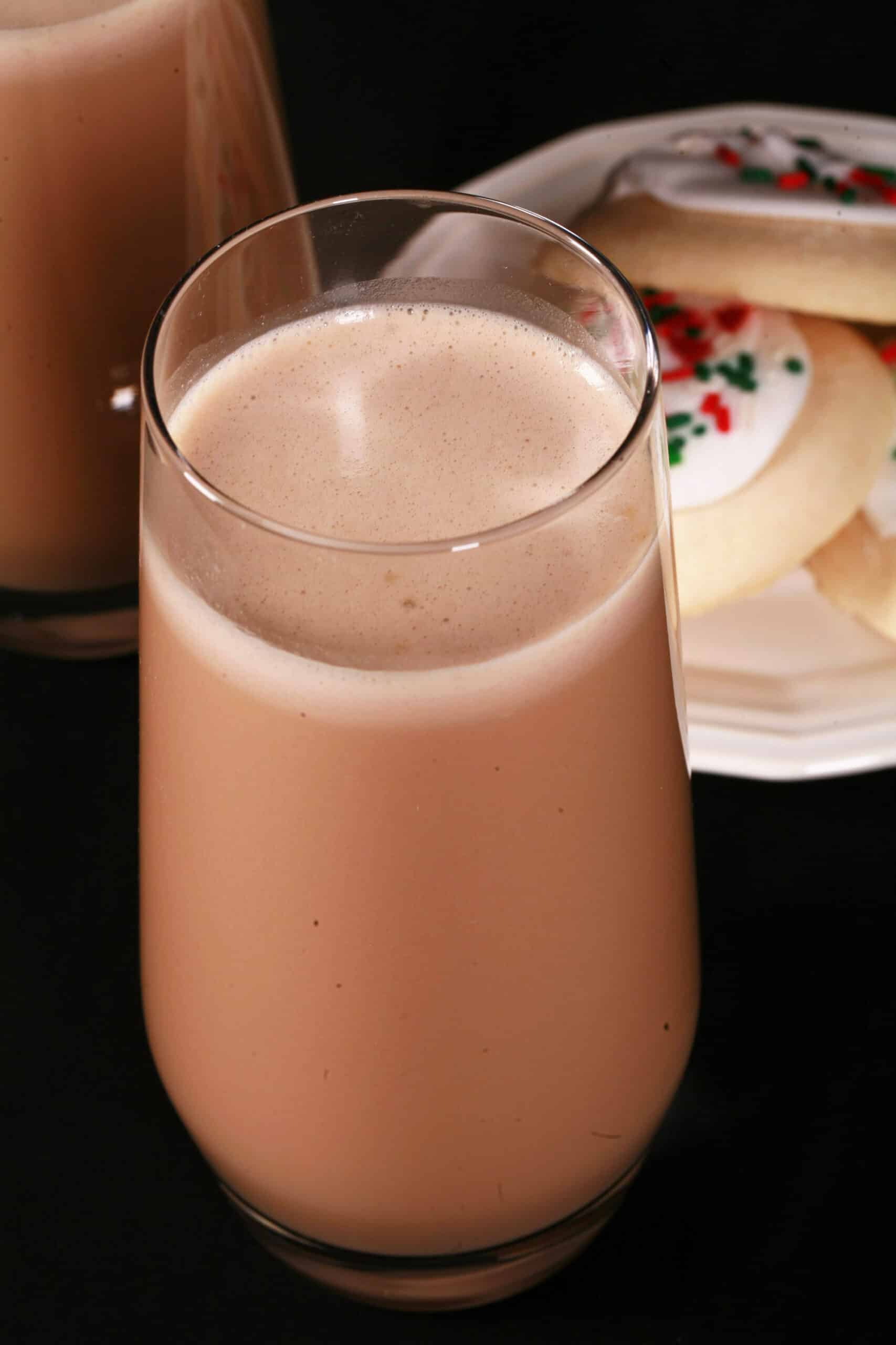 2 tall glasses of sugar cookie protein shakes, with frosted sugar cookies on a plate next to them.