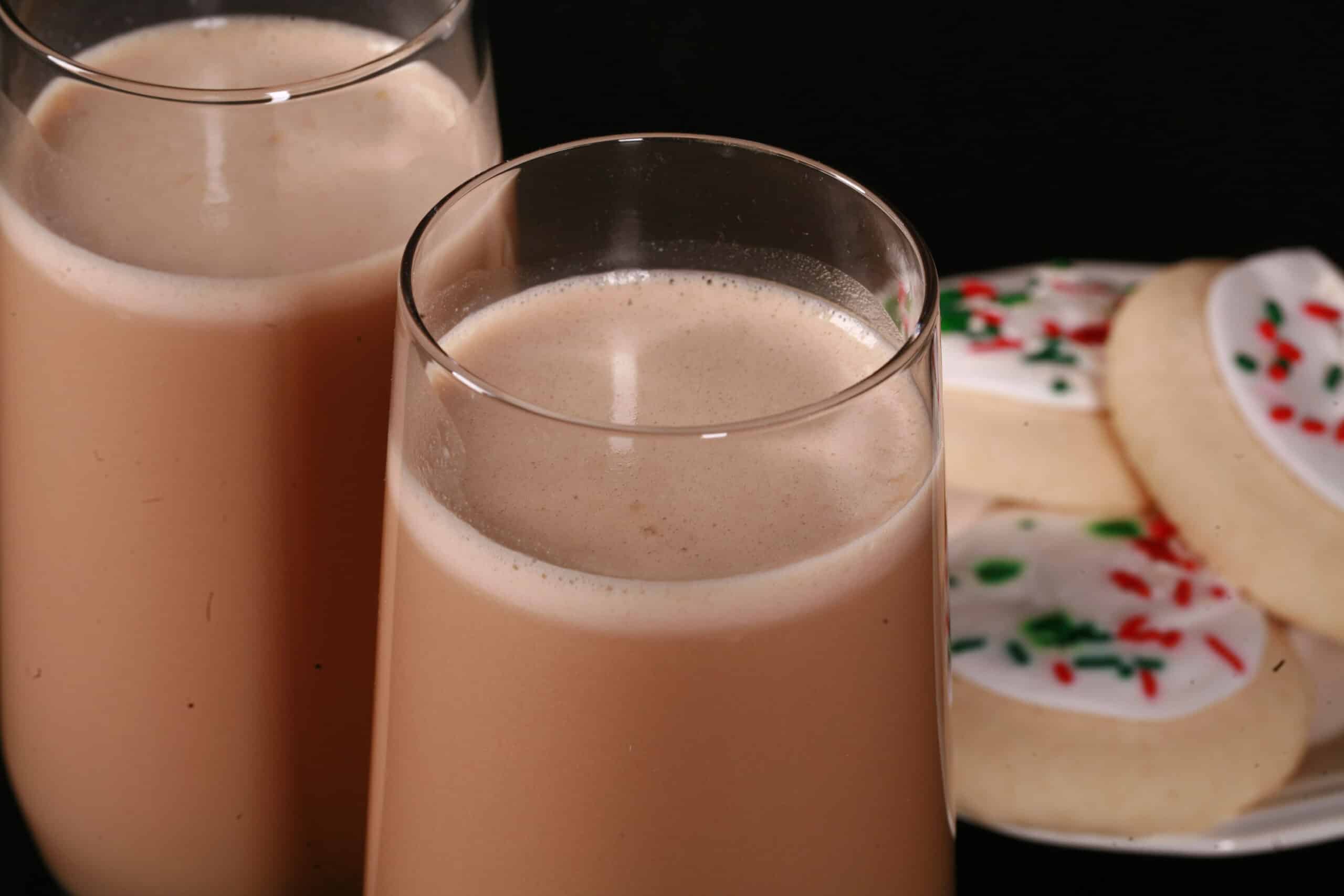 2 tall glasses of sugar cookie flavoured protein coffee shake, with frosted sugar cookies on a plate next to them.