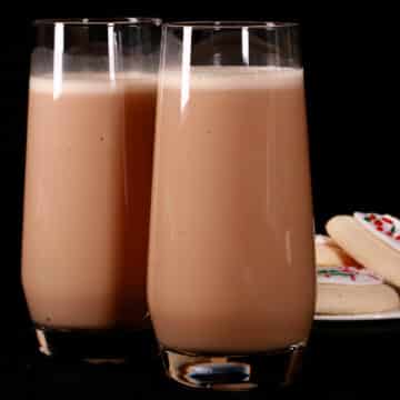 2 tall glasses of sugar cookie protein shakes, with frosted sugar cookies on a plate next to them.