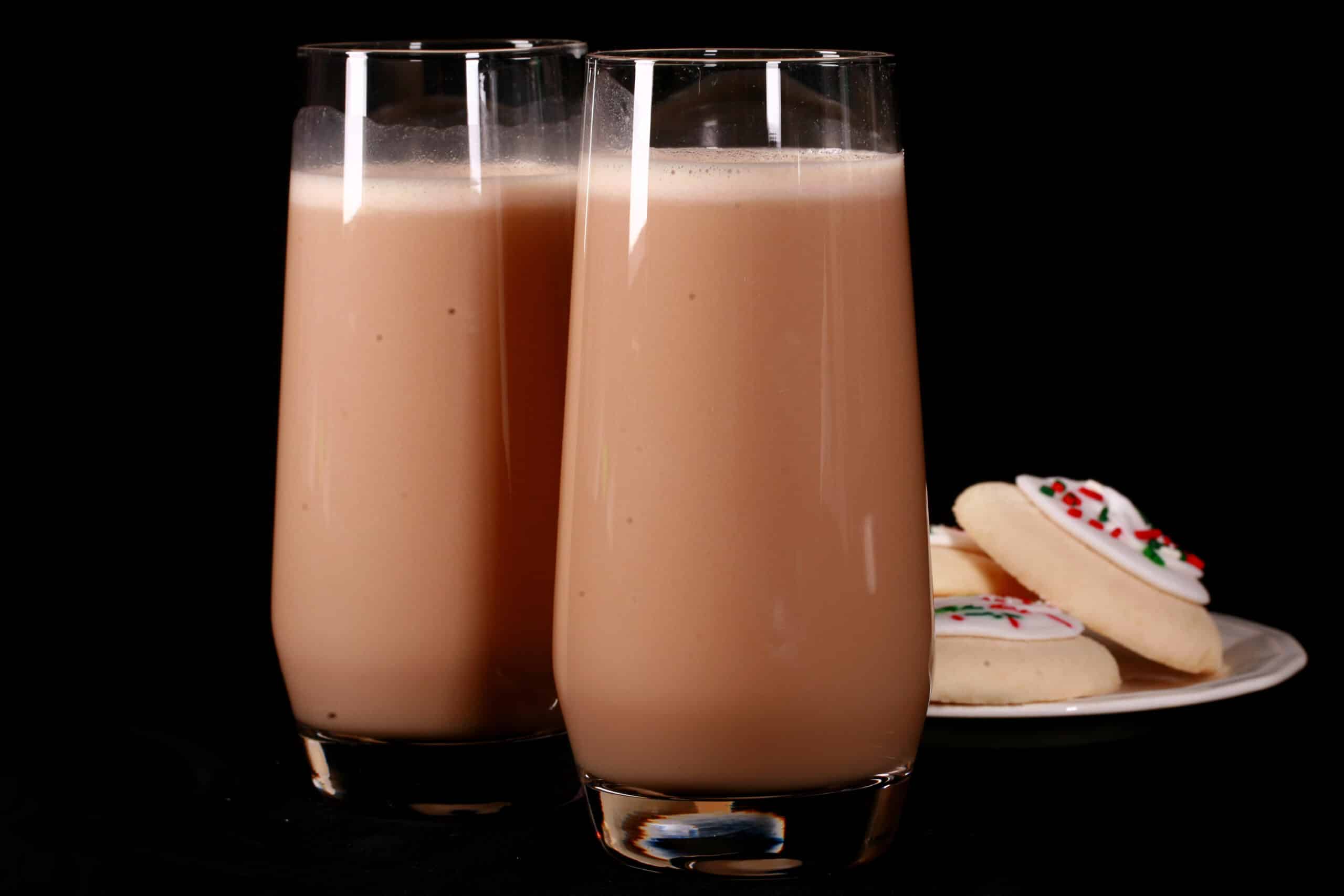2 tall glasses of sugar cookie protein shakes, with frosted sugar cookies on a plate next to them.