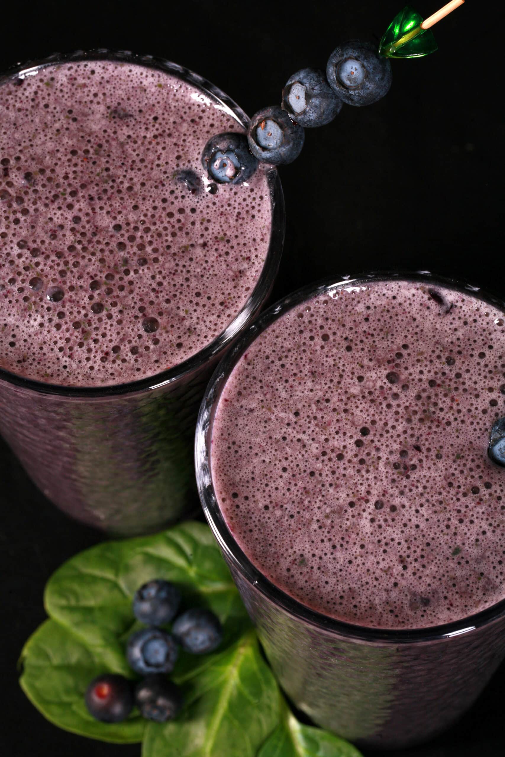 2 tall glasses of high protein blueberry spinach smoothies, garnished with fresh blueberries and baby spinach.