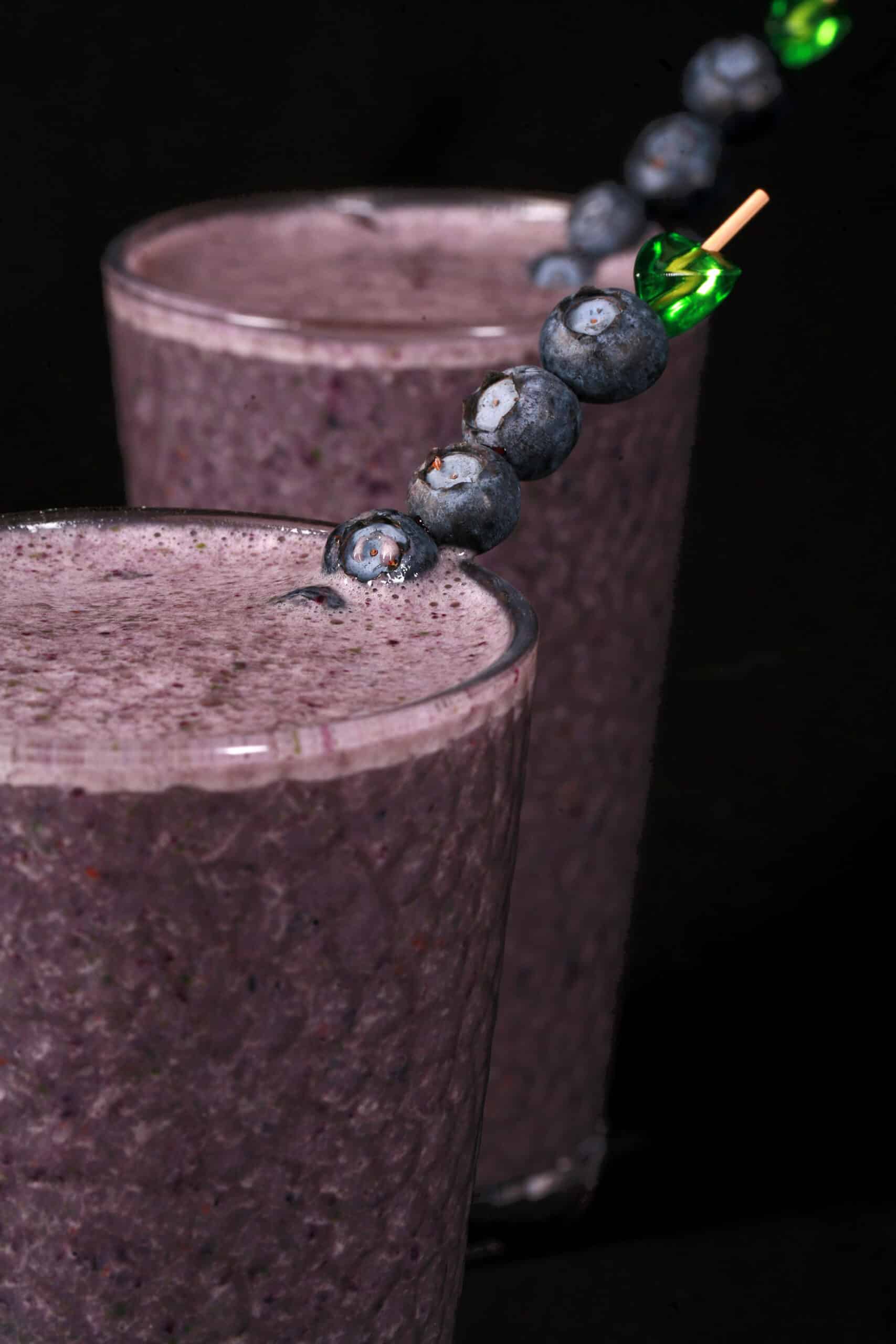 2 tall glasses of high protein blueberry spinach smoothie, garnished with fresh blueberries and baby spinach.
