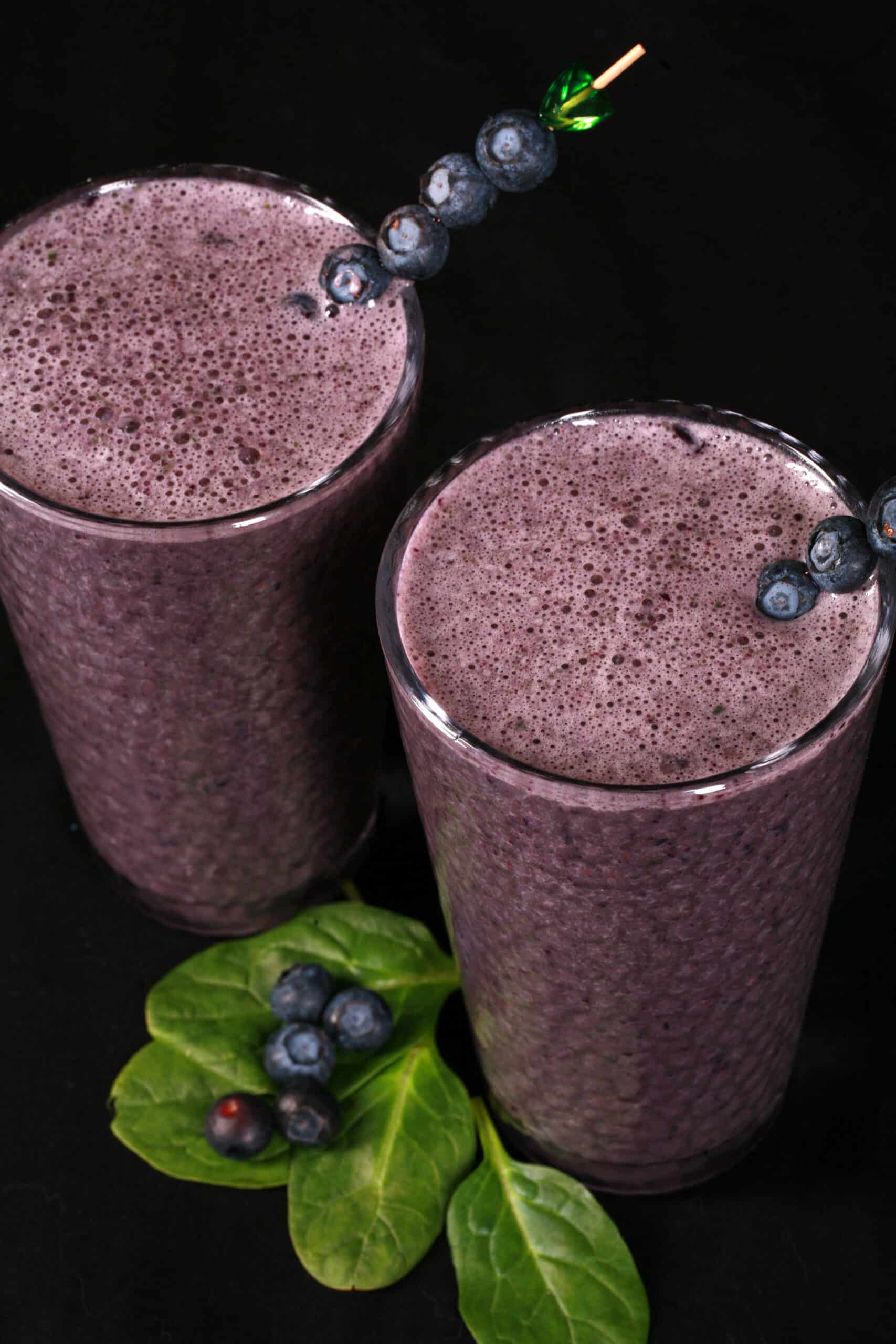 2 tall glasses of high protein blueberry spinach smoothies, garnished with fresh blueberries and baby spinach.