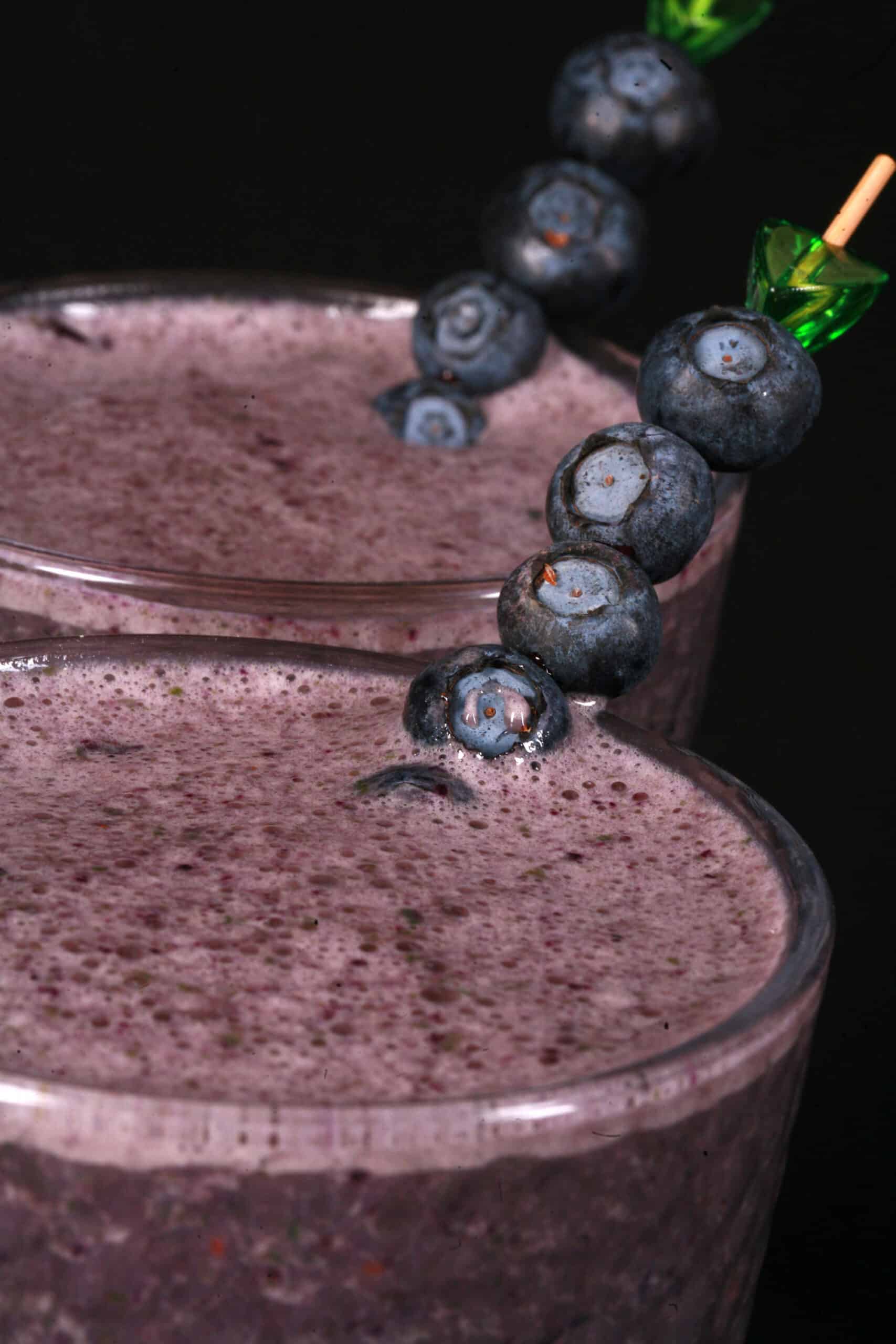 2 tall glasses of high protein blueberry spinach smoothie, garnished with fresh blueberries and baby spinach.