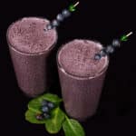 2 tall glasses of high protein blueberry spinach smoothie, garnished with fresh blueberries and baby spinach.