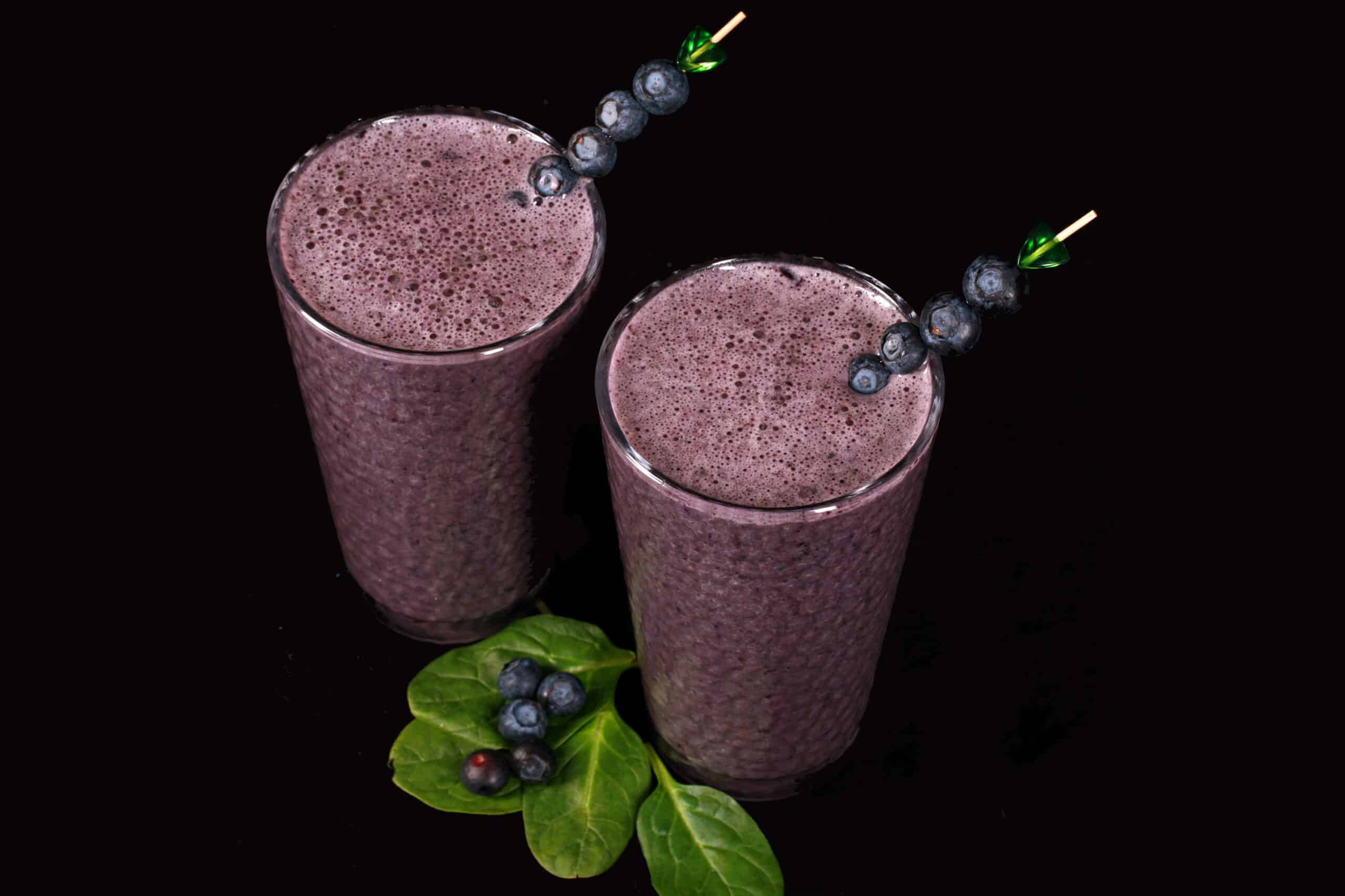 2 tall glasses of high protein blueberry spinach smoothie, garnished with fresh blueberries and baby spinach.