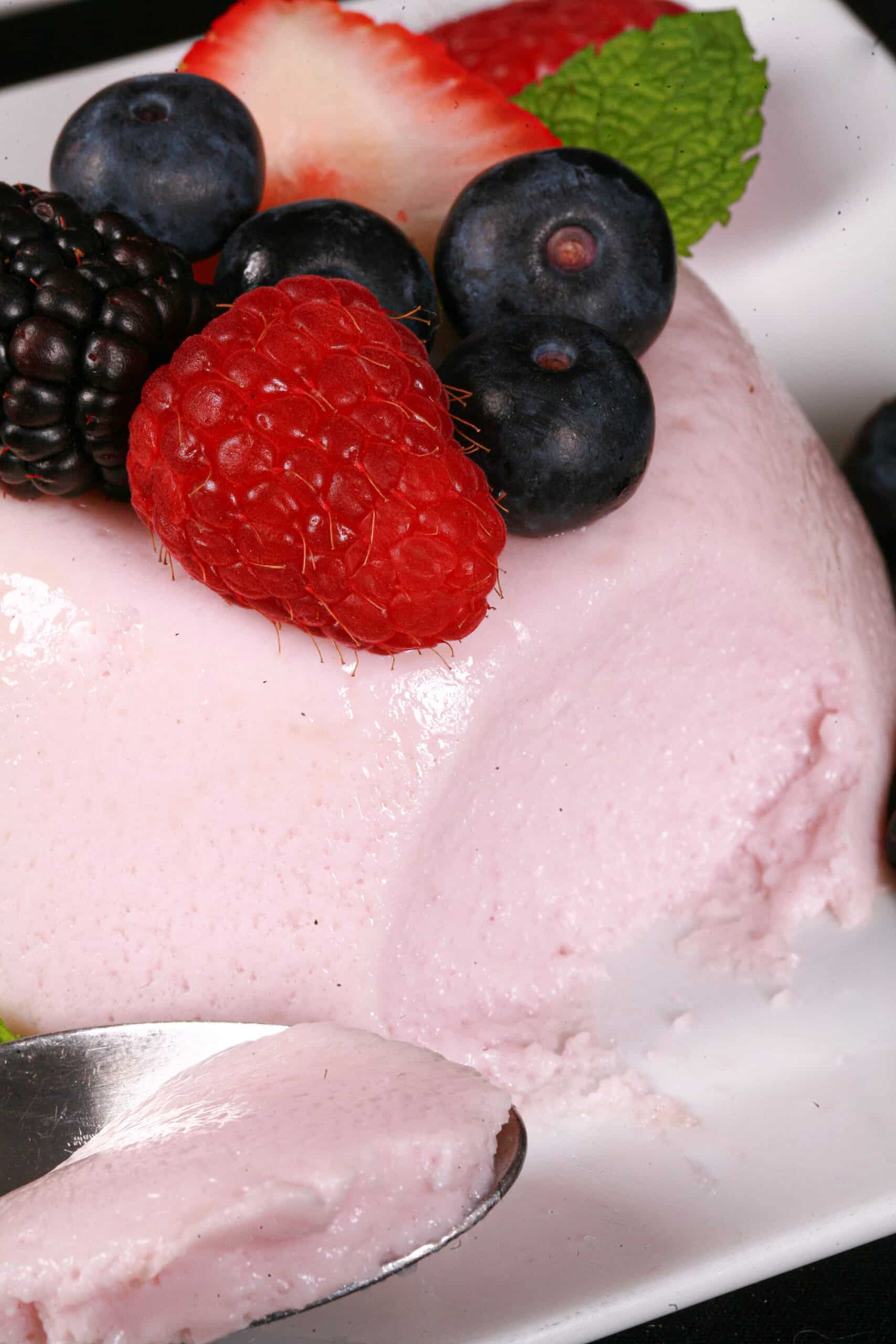 A light pink protein powder panna cotta on a plate, with mixed berries and mint leaves.