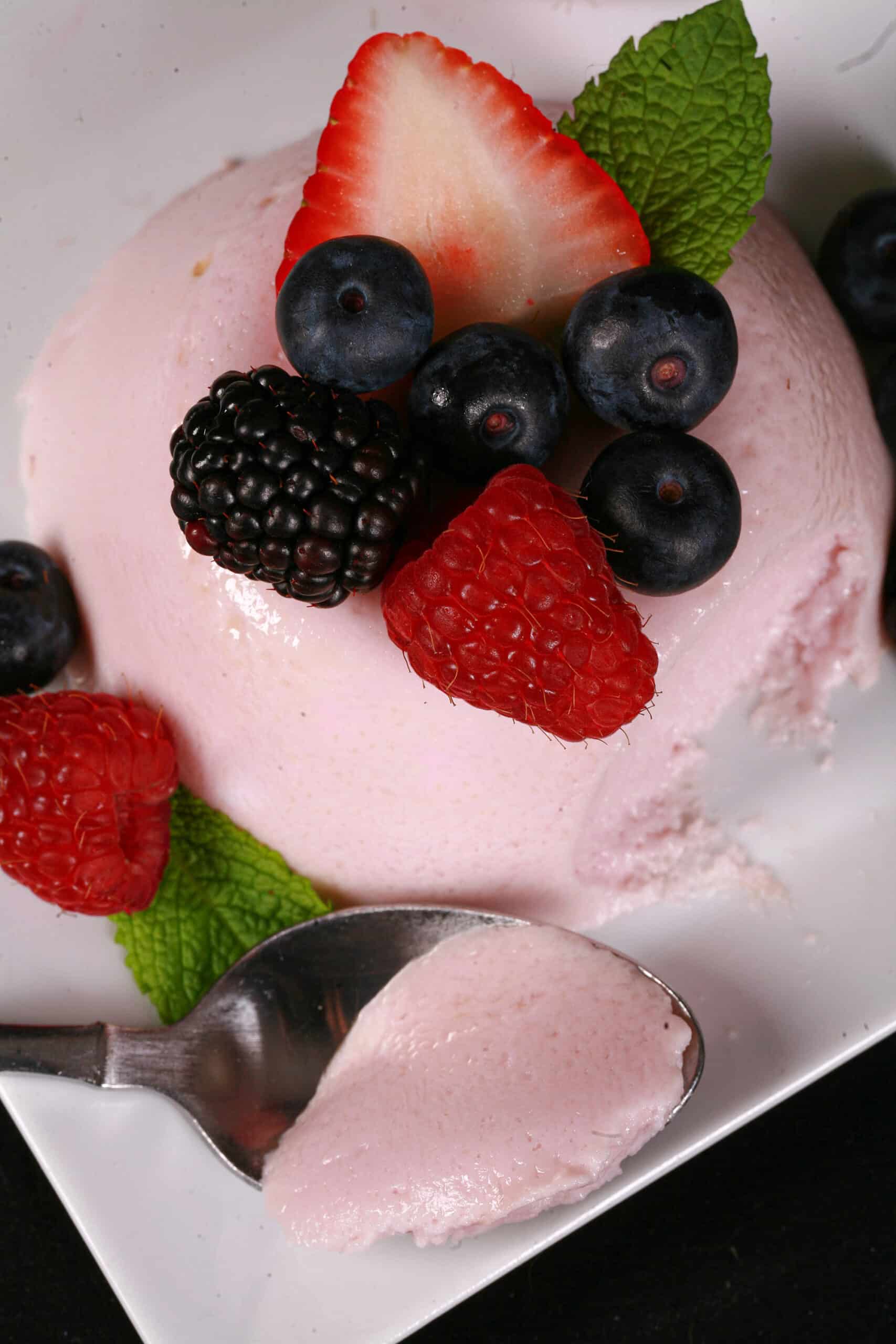 A light pink protein powder panna cotta on a plate, with mixed berries and mint leaves.
