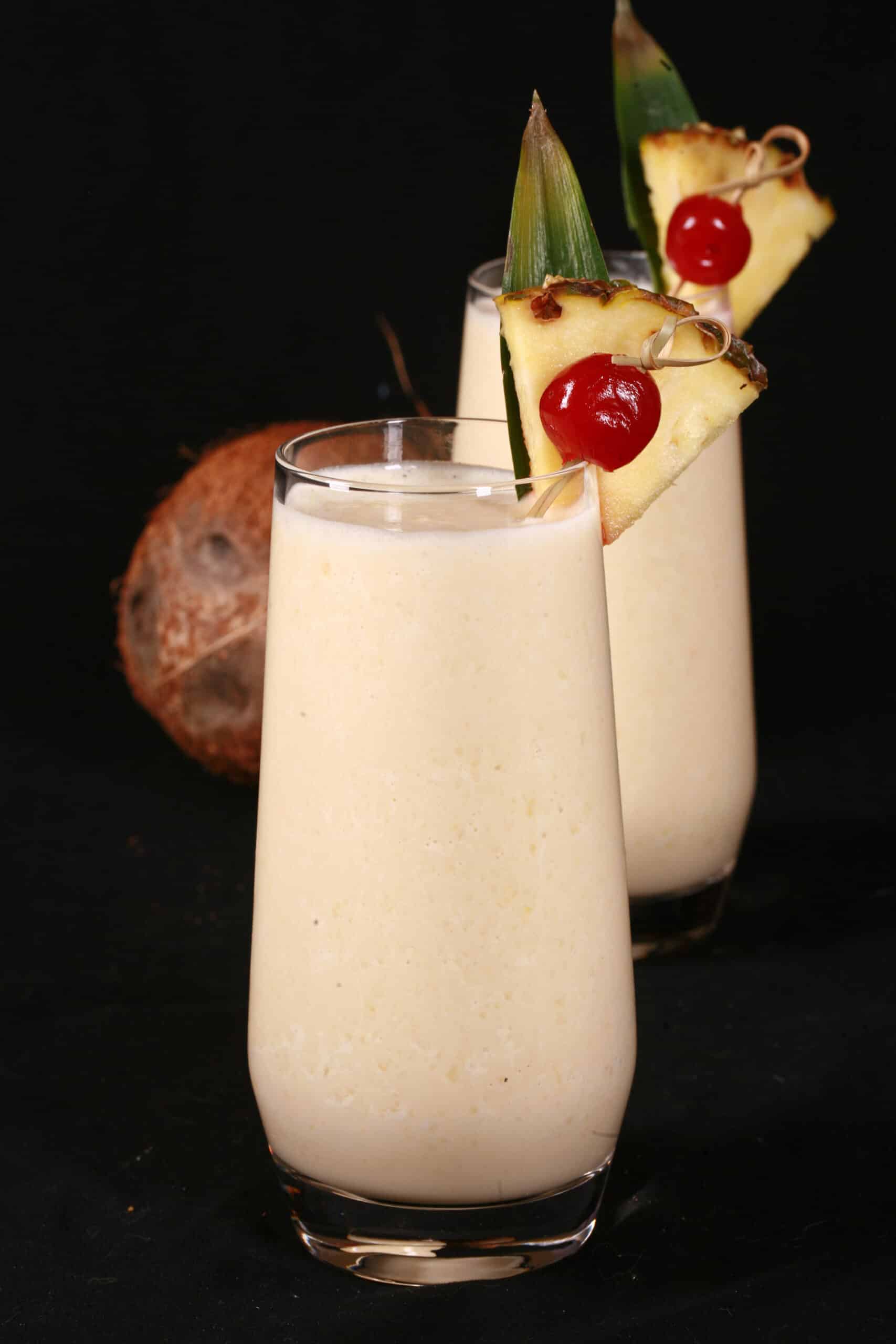 2 High Protein Pina Colada Smoothies garnished with a pineapple wedge and cherry.