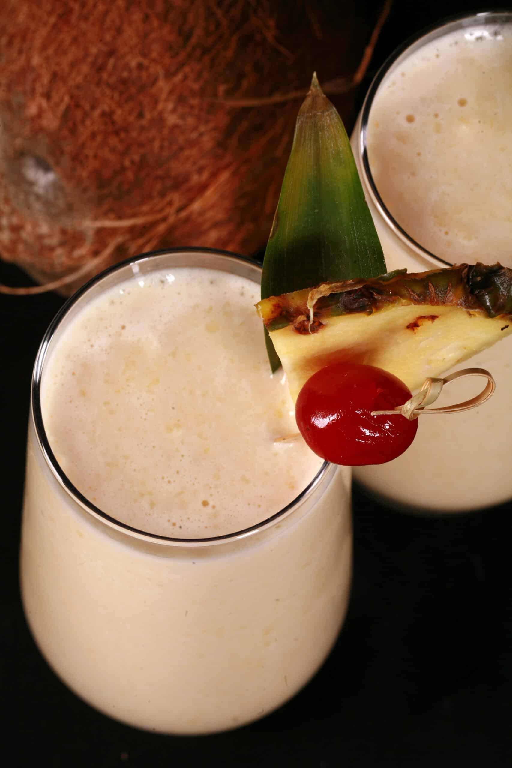 2 Pina Colada Protein Smoothies garnished with a pineapple wedge and cherry.
