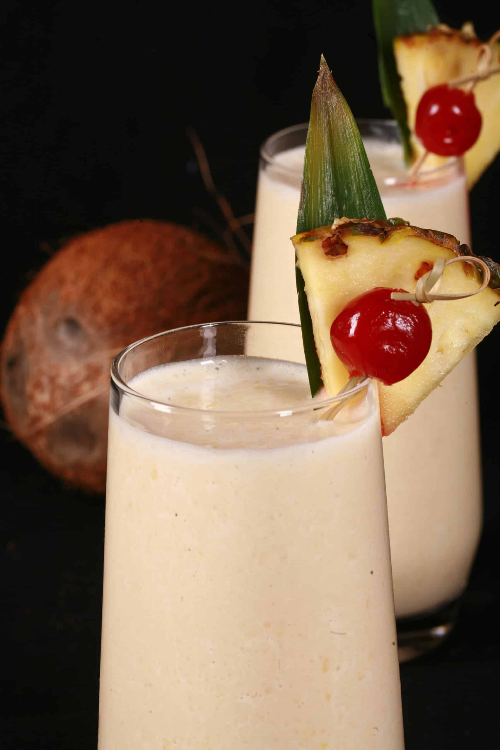 2 Pina Colada Protein Smoothies garnished with a pineapple wedge and cherry.