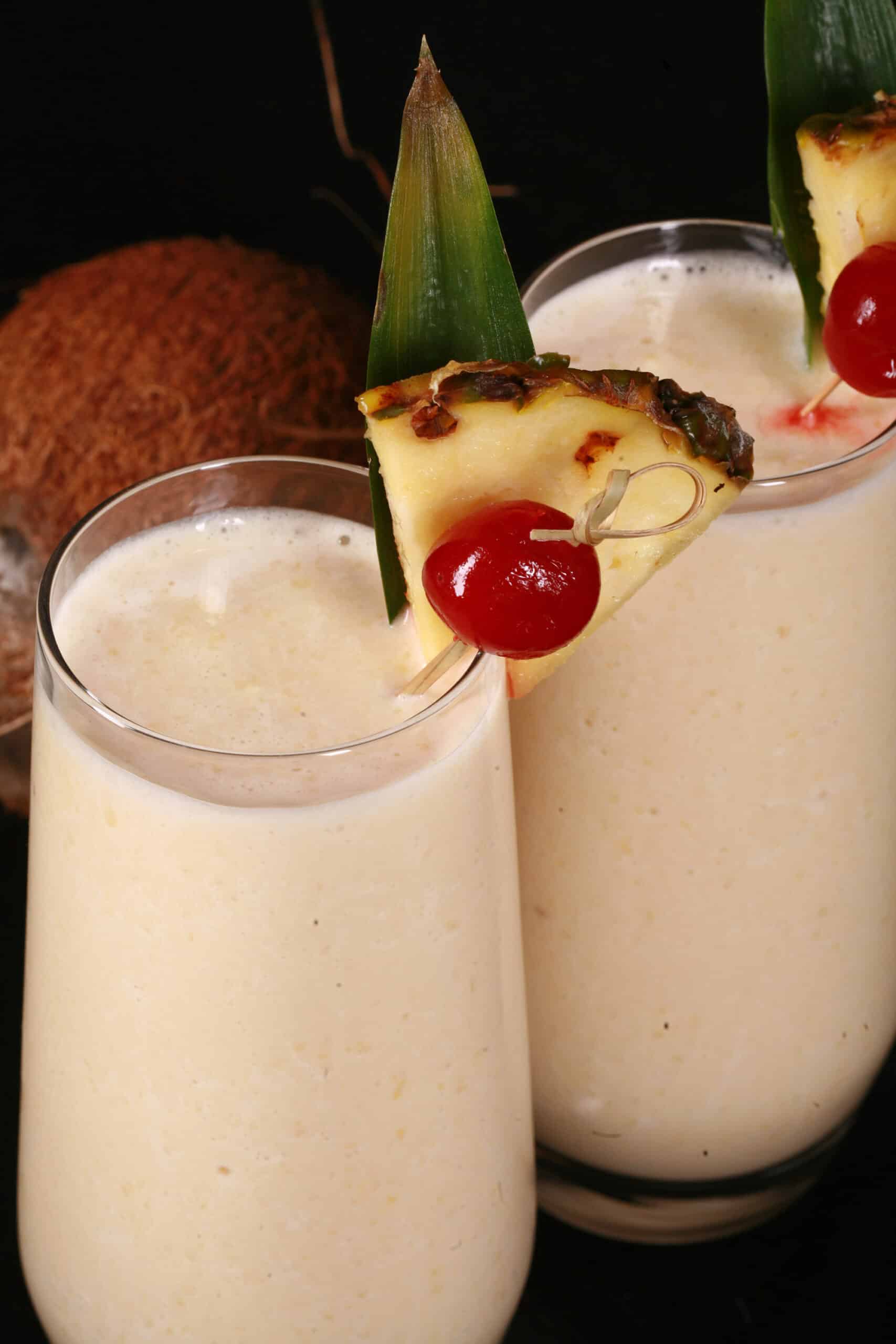 2 High Protein Pina Colada Smoothies garnished with a pineapple wedge and cherry.