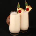 2 Pina Colada Protein Smoothies garnished with a pineapple wedge and cherry.