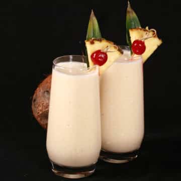 2 Pina Colada Protein Smoothies garnished with a pineapple wedge and cherry.
