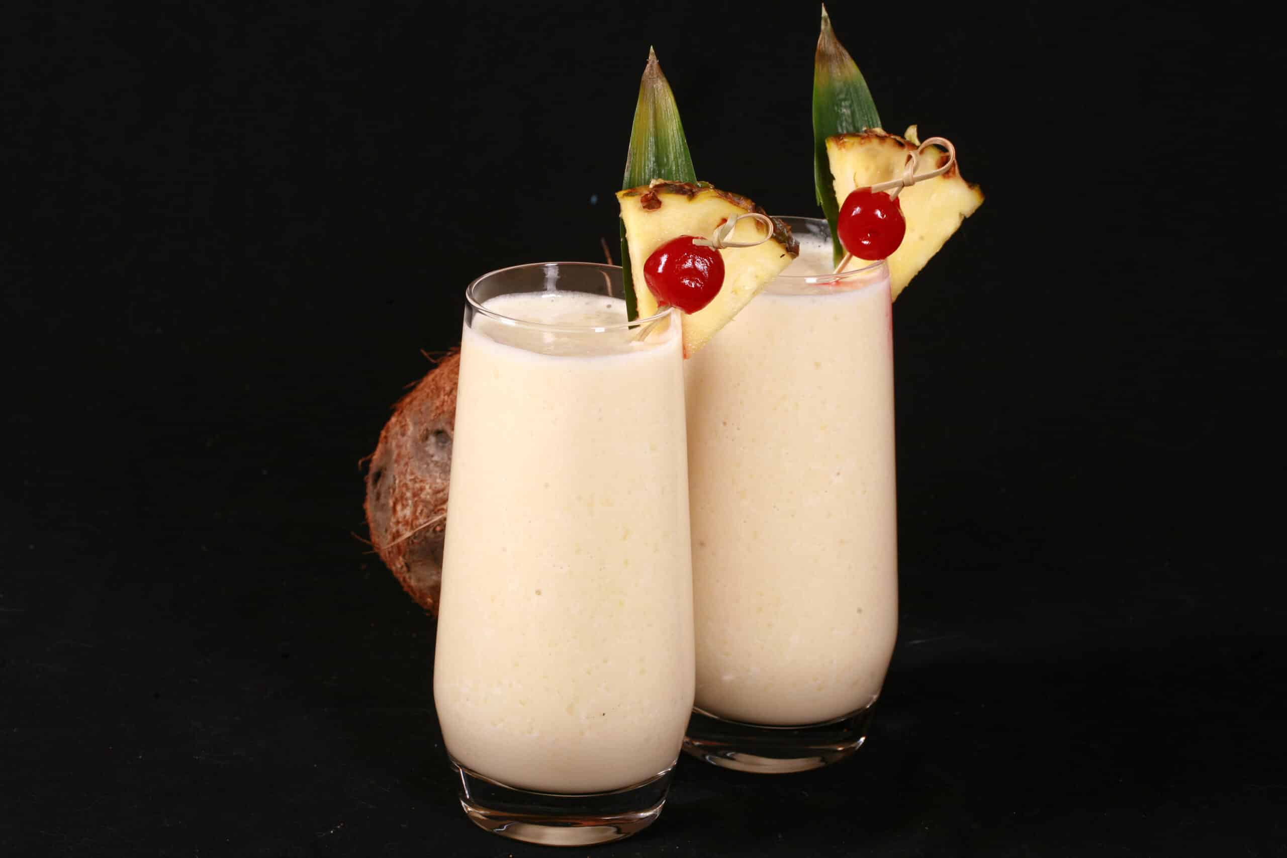 2 Pina Colada Protein Smoothies garnished with a pineapple wedge and cherry.
