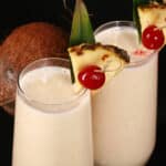 2 High Protein Pina Colada Smoothies garnished with a pineapple wedge and cherry.