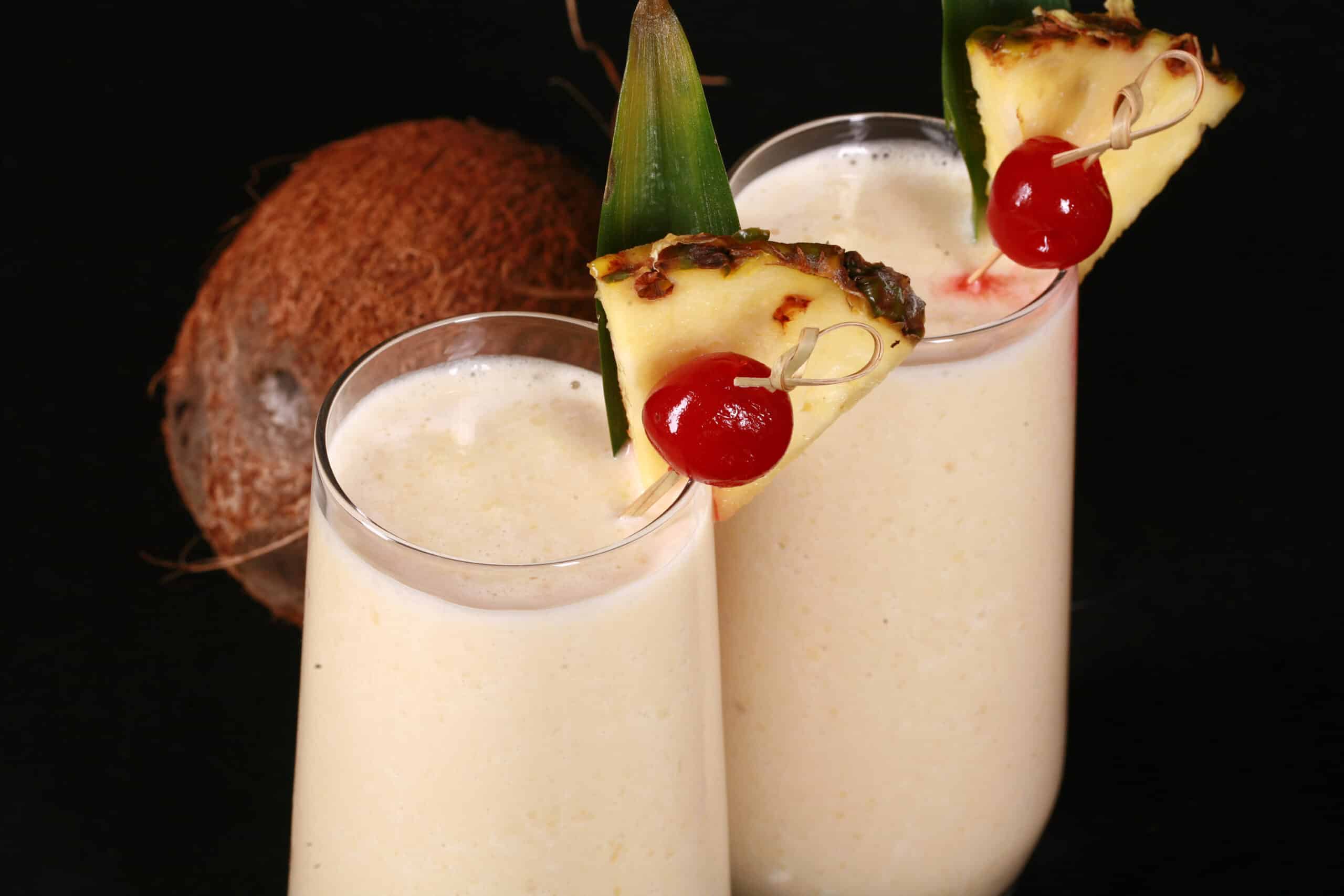 2 High Protein Pina Colada Smoothies garnished with a pineapple wedge and cherry.