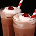 2 tall glasses of root beer float flavoured protein shakes, topped with whipped cream and a maraschino cherry.
