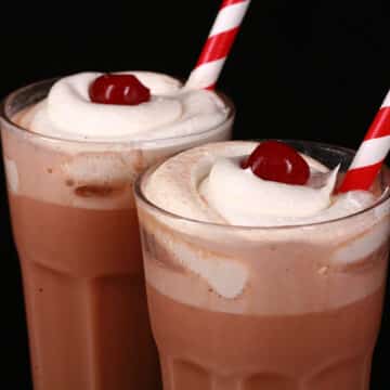 2 tall glasses of root beer float flavoured protein shakes, topped with whipped cream and a maraschino cherry.