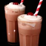 2 tall glasses of root beer float protein shakes, topped with whipped cream and a maraschino cherry.