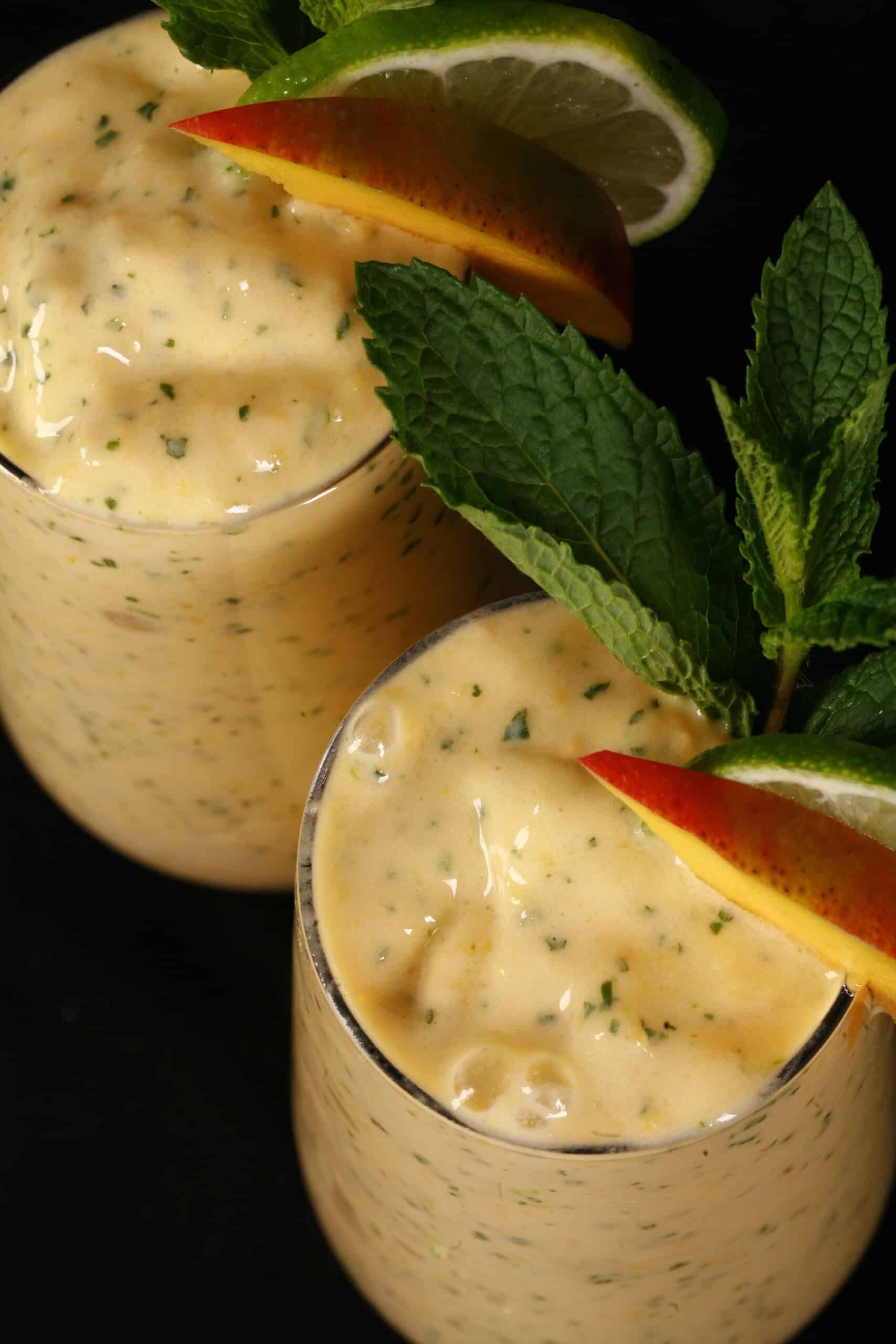 2 mango mojito protein smoothies, garnished with fresh mango and lime slices and a mint sprig.