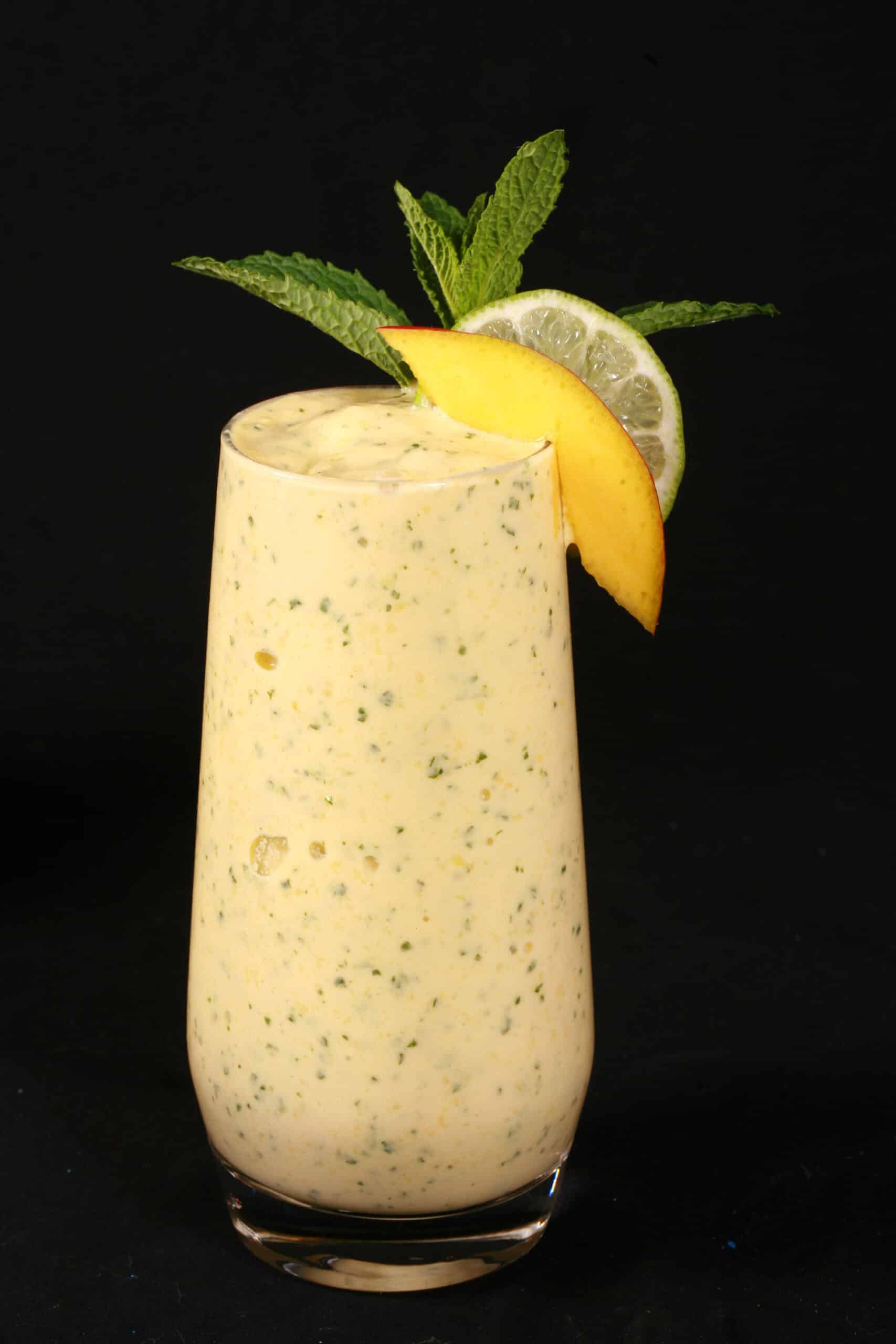 A mango mojito protein smoothie, garnished with fresh mango and lime slices and a mint sprig.