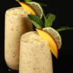 2 mango mojito protein smoothies, garnished with fresh mango and lime slices and a mint sprig.