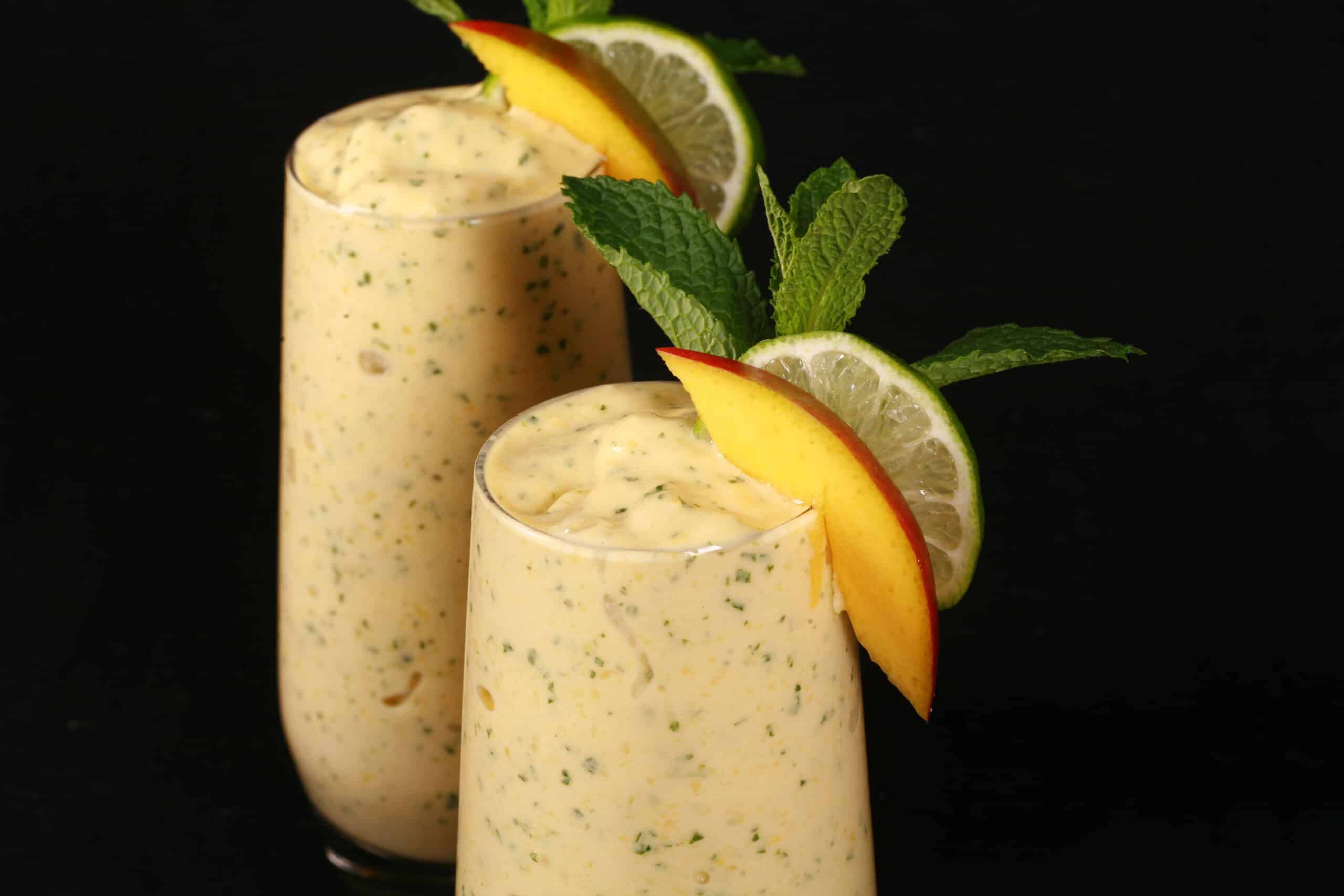 2 mango mojito protein smoothies, garnished with fresh mango and lime slices and a mint sprig.