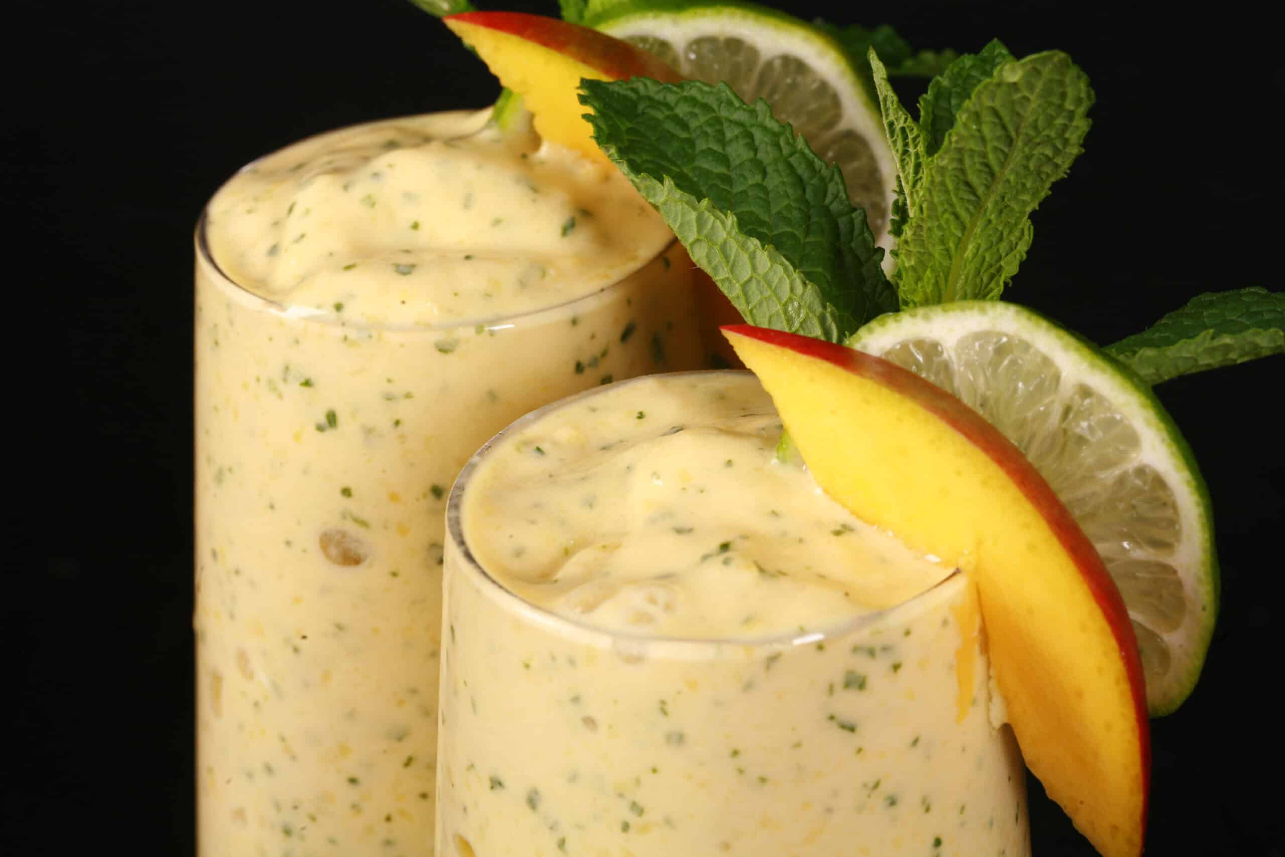 2 high protein mango mojito smoothies, garnished with fresh mango and lime slices and a mint sprig.