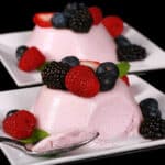 2 light pink high protein panna cotta servings on plates, with mixed berries and mint leaves.