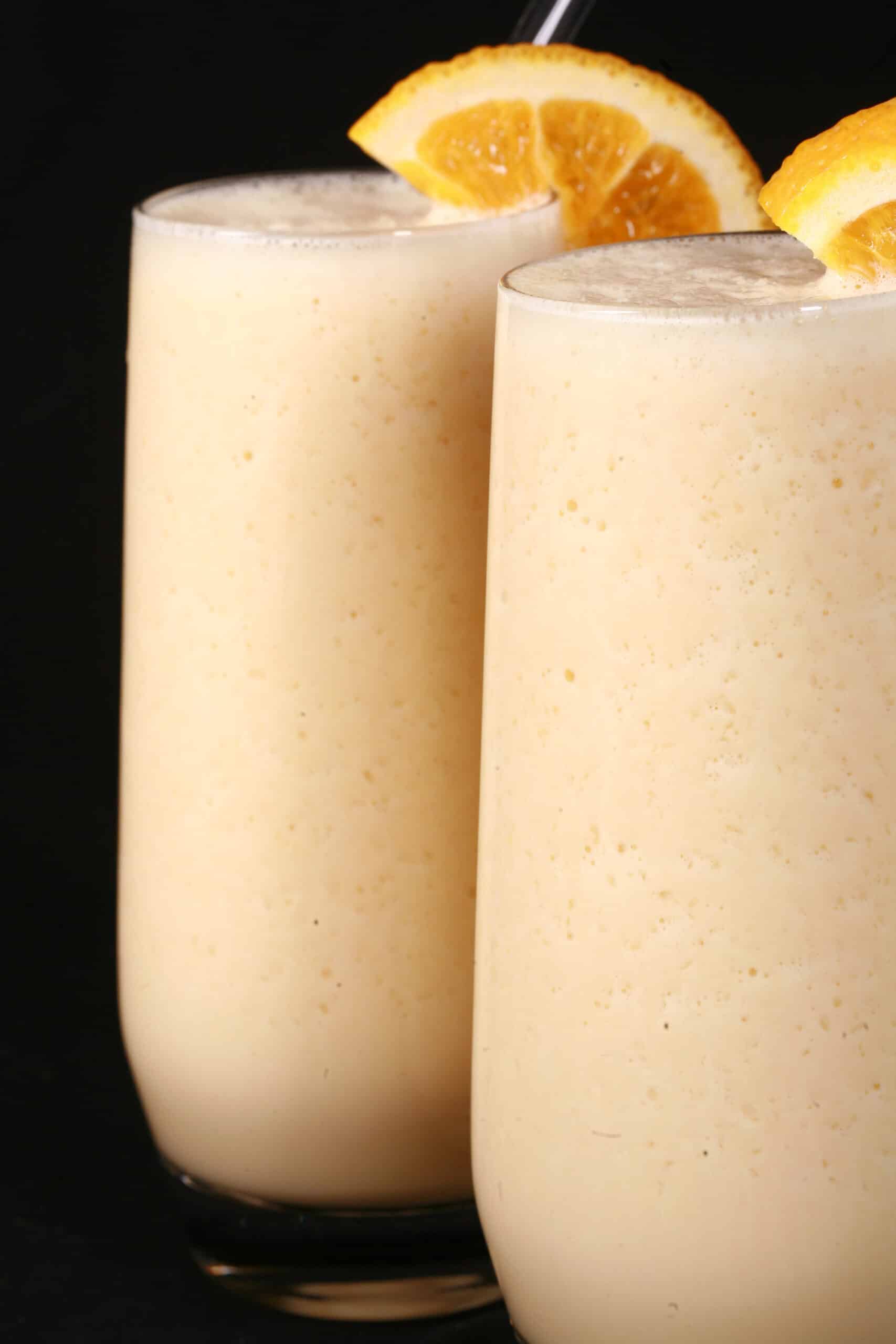 Two tall glasses of protein powder Orange Julius smoothies, garnished with fresh orange slices.