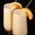 Two tall glasses of high protein Orange Julius smoothies, garnished with fresh orange slices