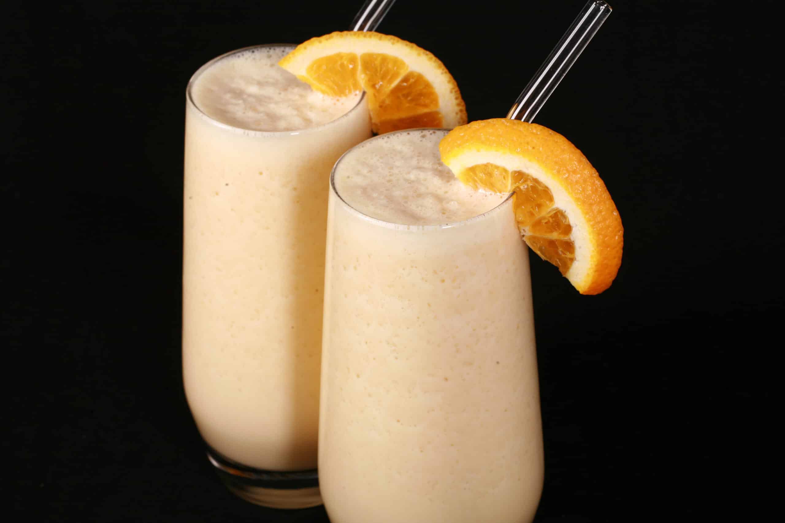 Two tall glasses of high protein Orange Julius smoothies, garnished with fresh orange slices