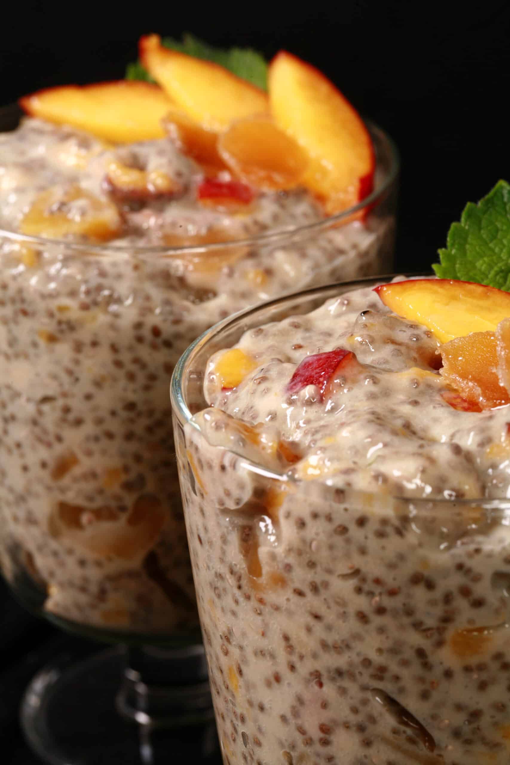 2 dessert glasses of high protein ginger peach chia pudding, garnished with peach slices, mint, and candied ginger.