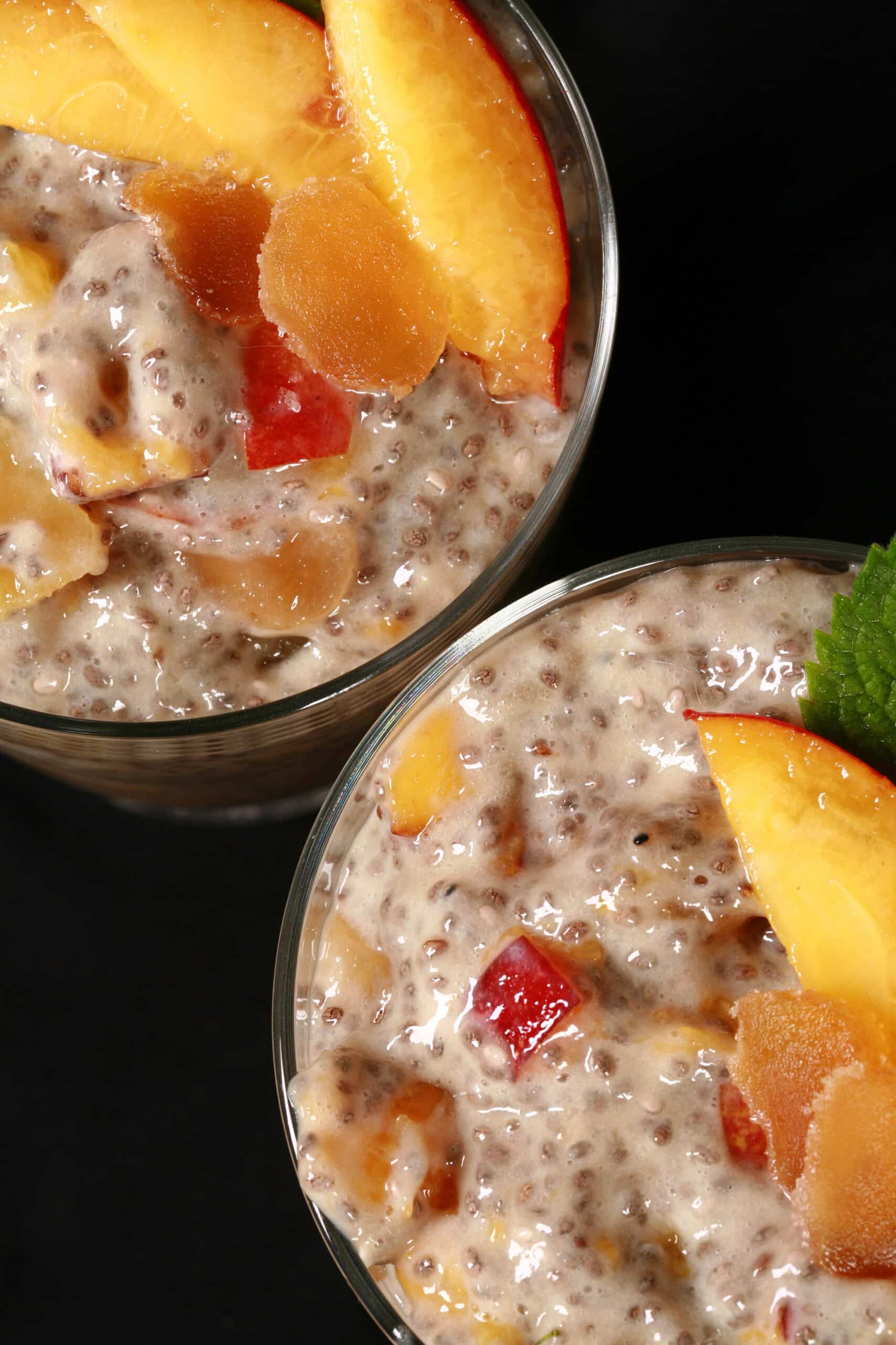 2 dessert glasses of high protein peach ginger chia pudding, garnished with peach slices, mint, and candied ginger.