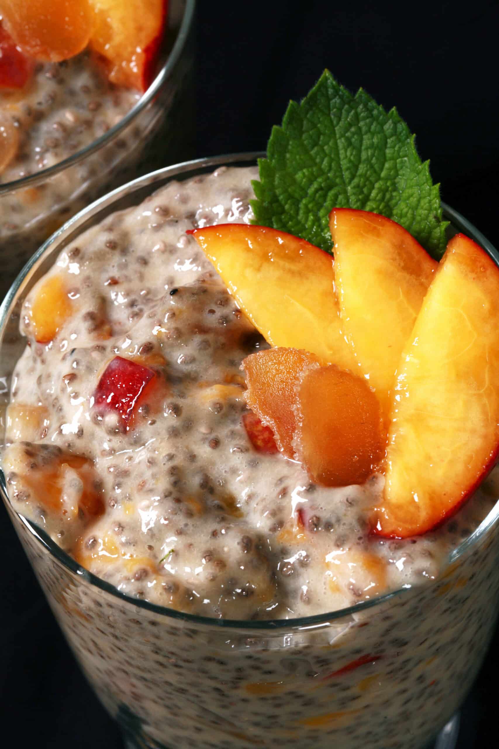 A dessert glass of high protein ginger peach chia pudding, garnished with peach slices, mint, and candied ginger.