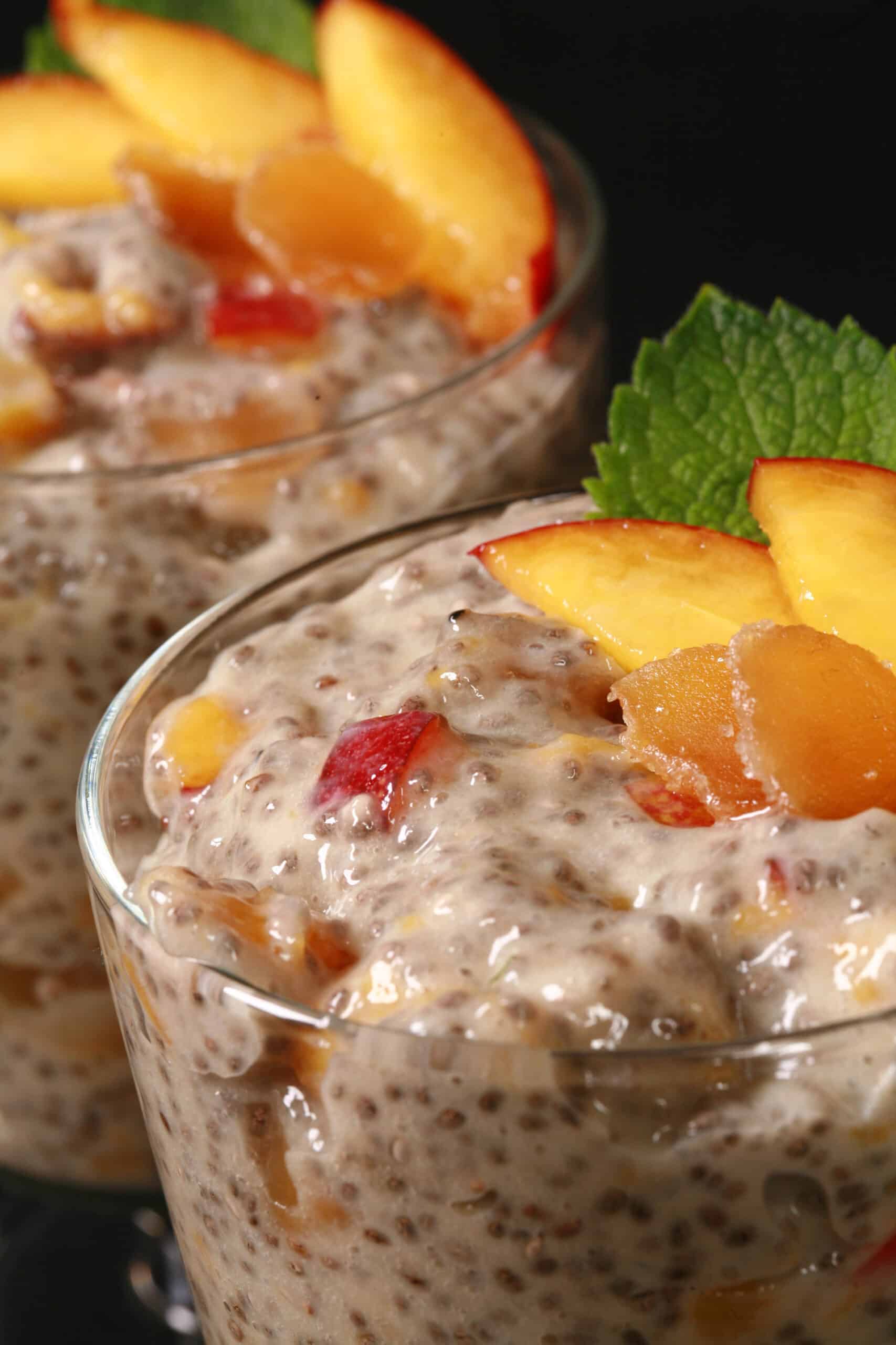 2 dessert glasses of high protein peach ginger chia pudding, garnished with peach slices, mint, and candied ginger.