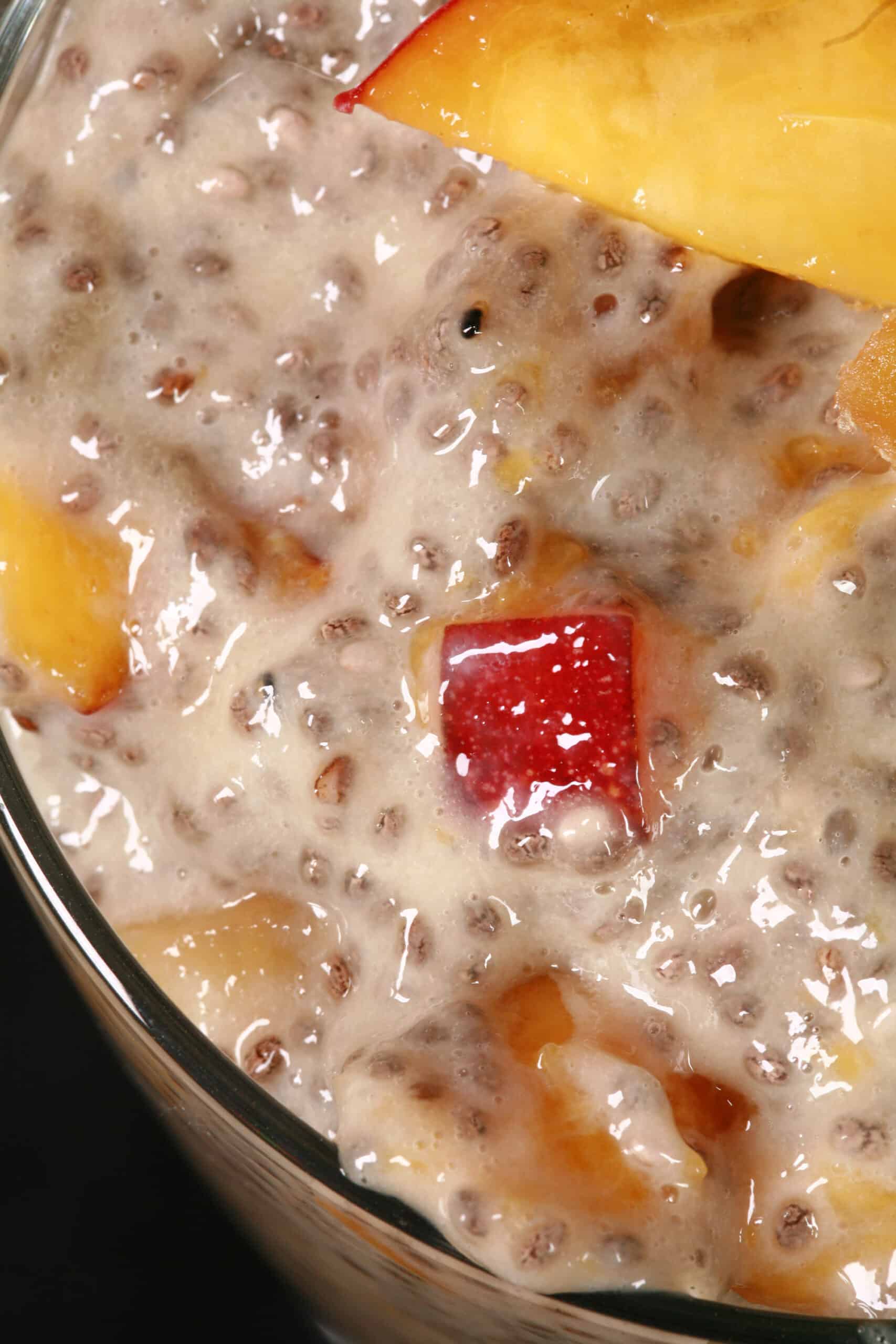 A dessert glass of high protein ginger peach chia pudding, garnished with peach slices, mint, and candied ginger.