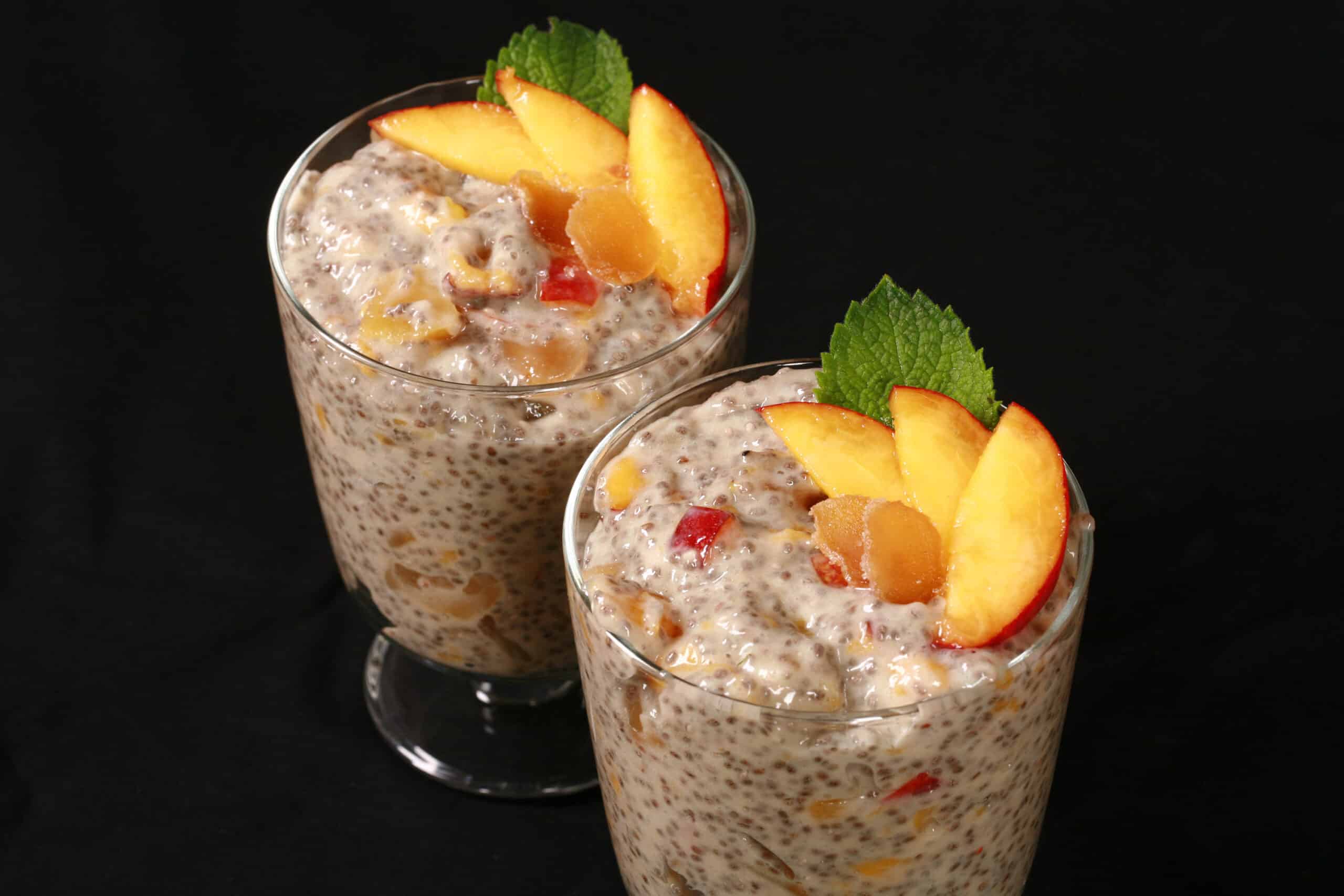 2 dessert glasses of high protein peach ginger chia pudding, garnished with peach slices, mint, and candied ginger.