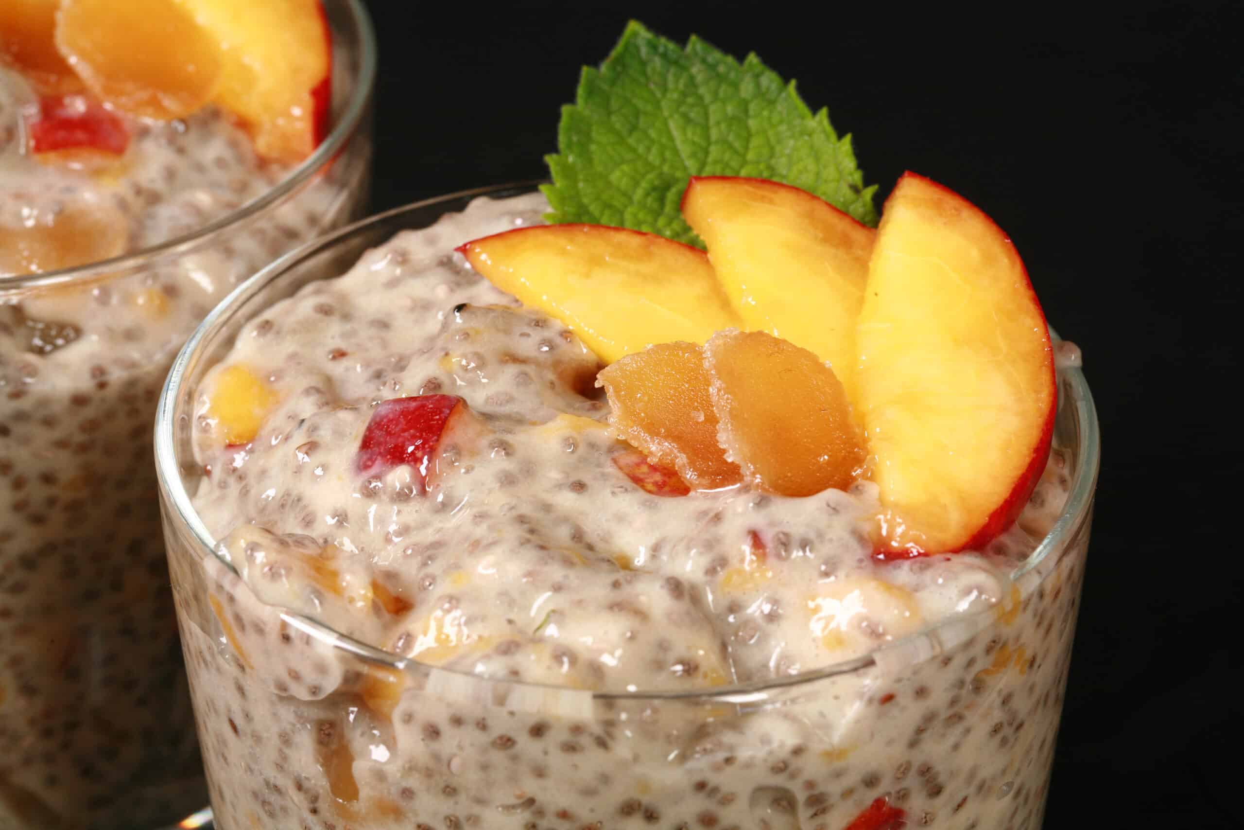 2 dessert glasses of high protein ginger peach chia pudding, garnished with peach slices, mint, and candied ginger.