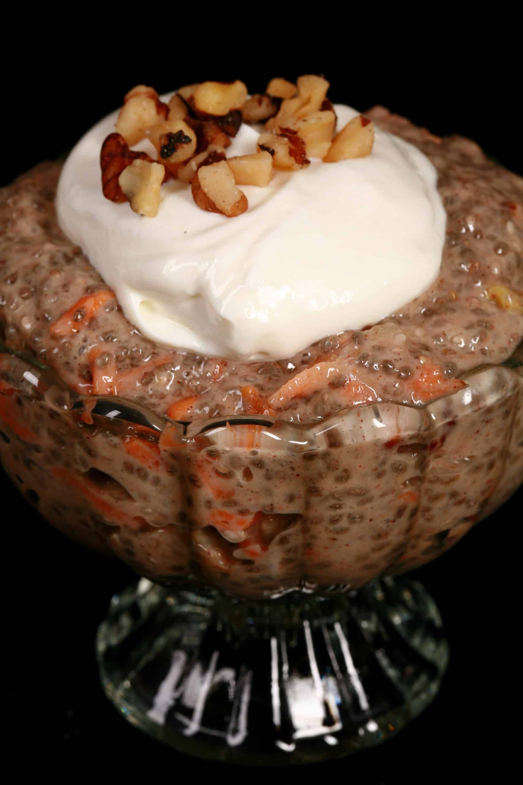 A dessert cup of high protein carrot cake chia pudding, topped with cream cheese Greek yogurt topping and chopped walnuts.