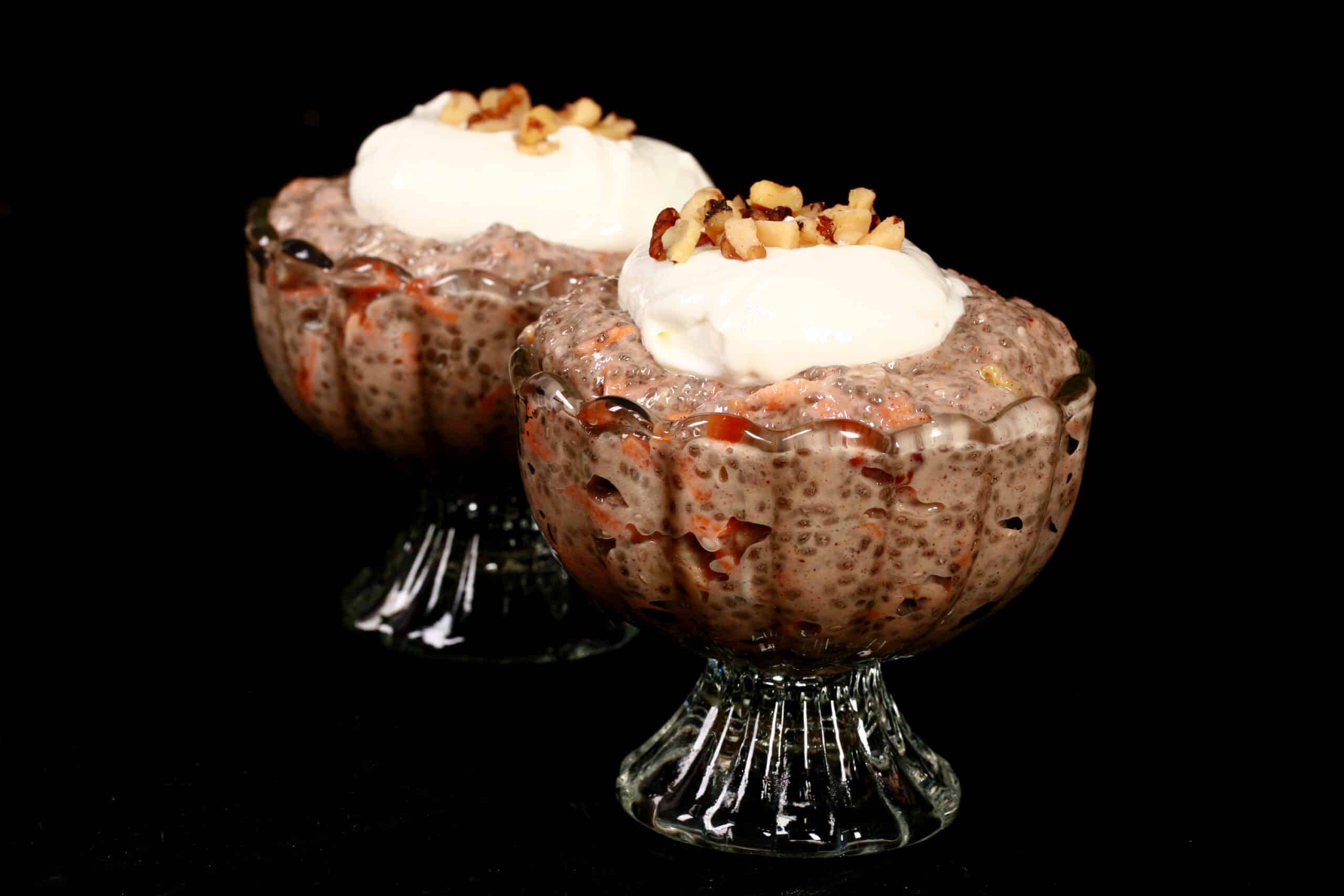 2 dessert cups of high protein carrot cake chia pudding, topped with cream cheese Greek yogurt topping and chopped walnuts.